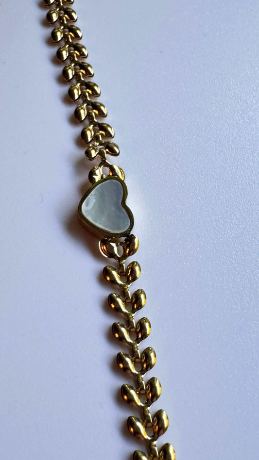 Gold bracelet with white heart-shaped charm on plain background