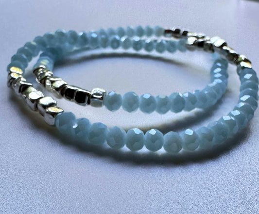 Light blue beaded bracelets with silver accents on a smooth white surface