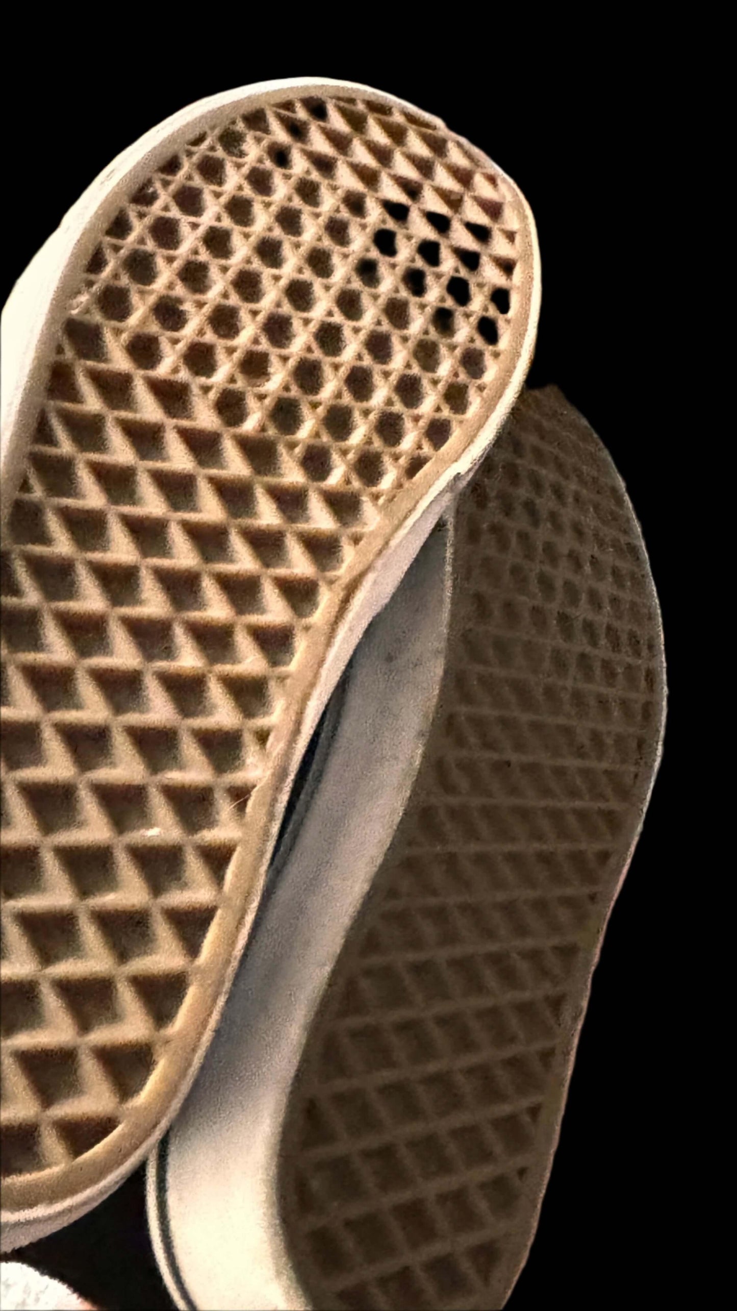 Close-up of worn waffle sole sneakers on black background, showing gum rubber texture