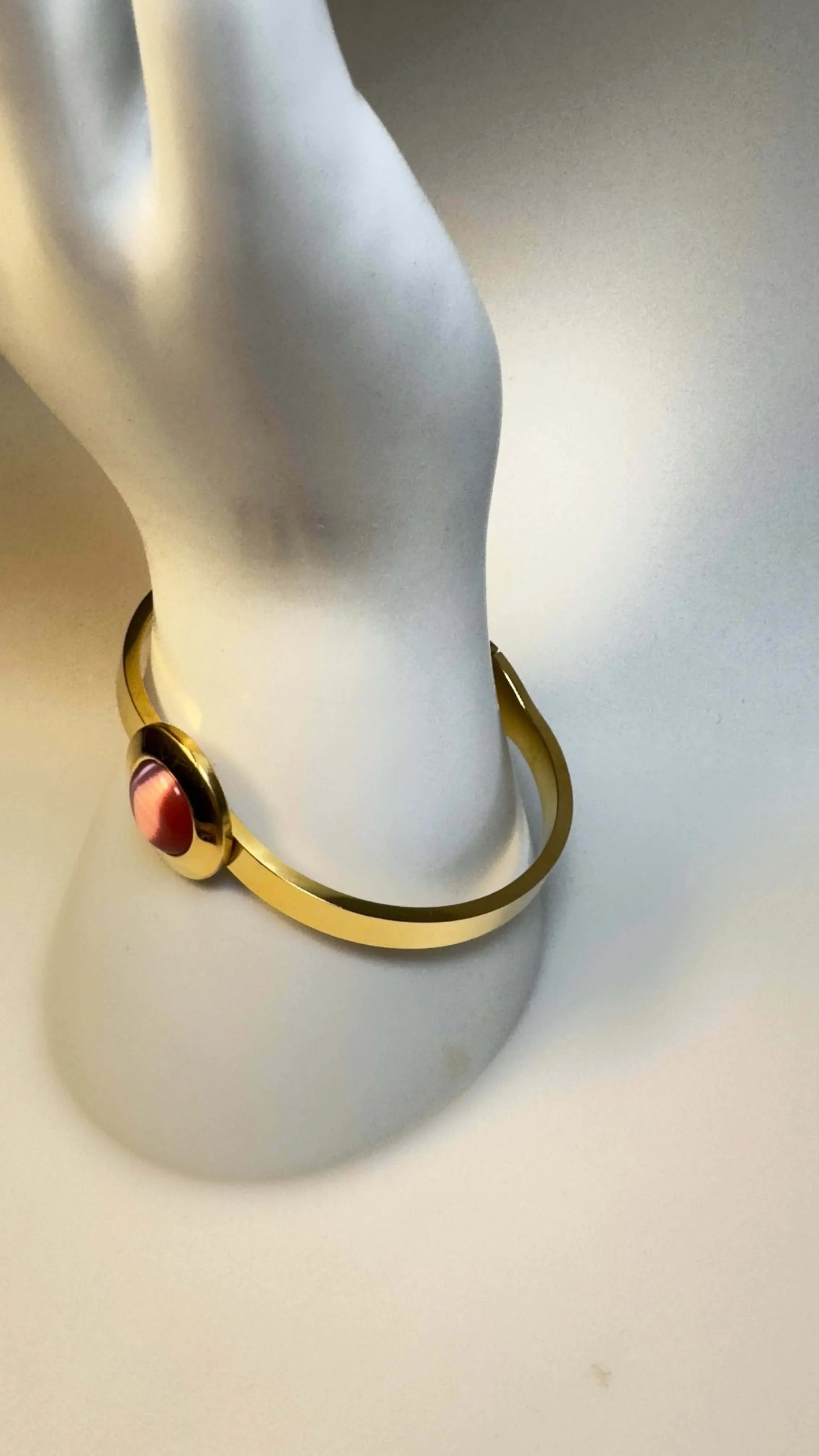 Pink gold bangle bracelet with round pink gemstone on white mannequin hand