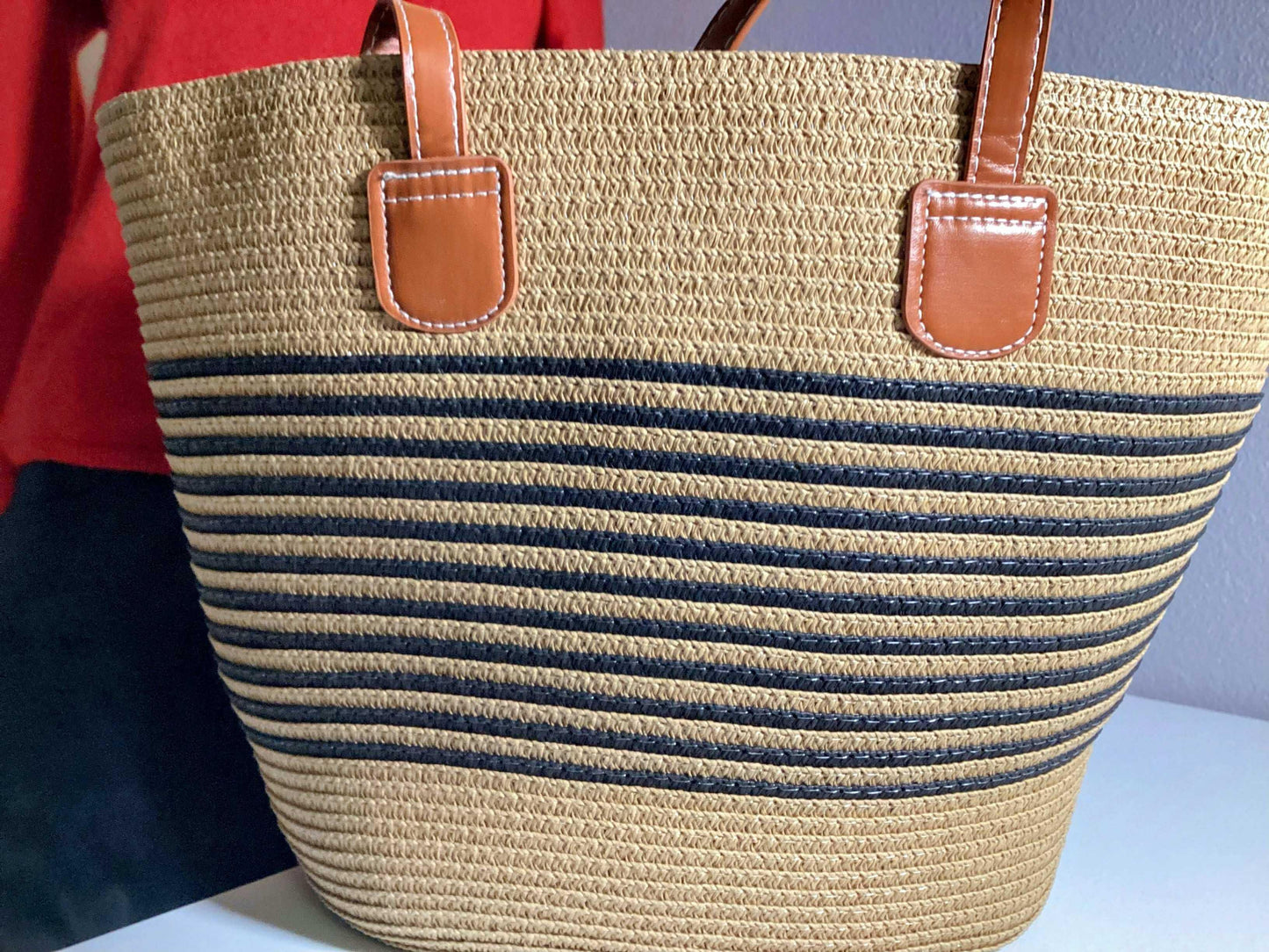 Straw beach bag with black horizontal stripes and brown leather handles on a table