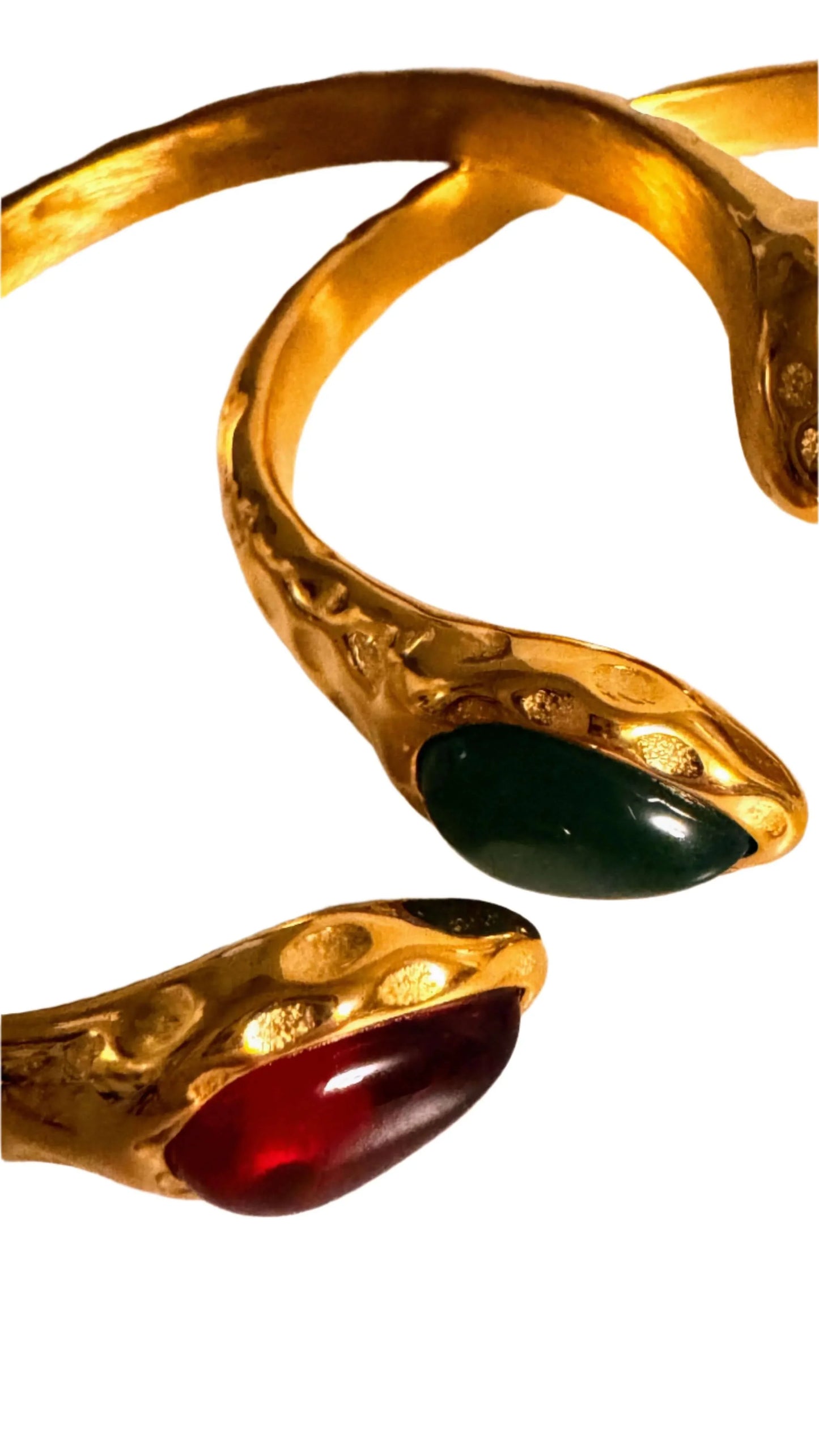 Close-up of gold snake bracelets with red and green gemstone heads on white background