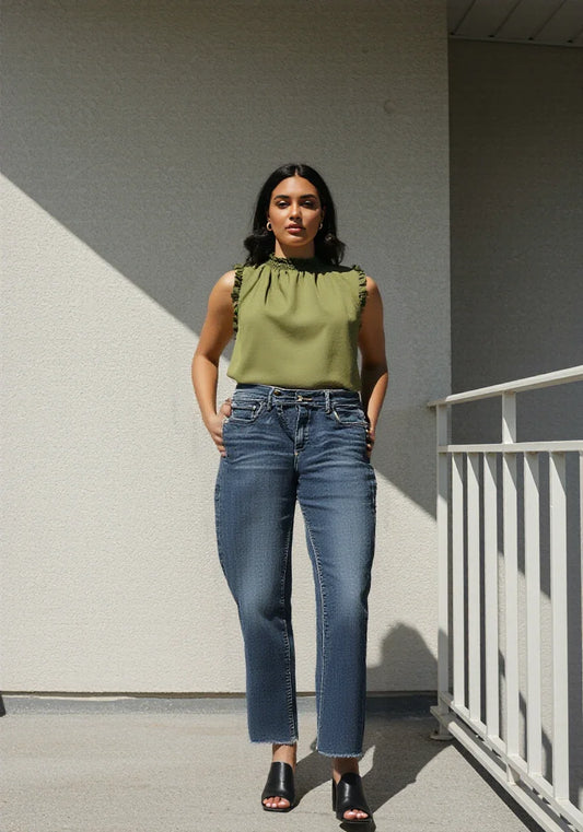 Woman wearing green sleeveless blouse and blue jeans standing on outdoor balcony