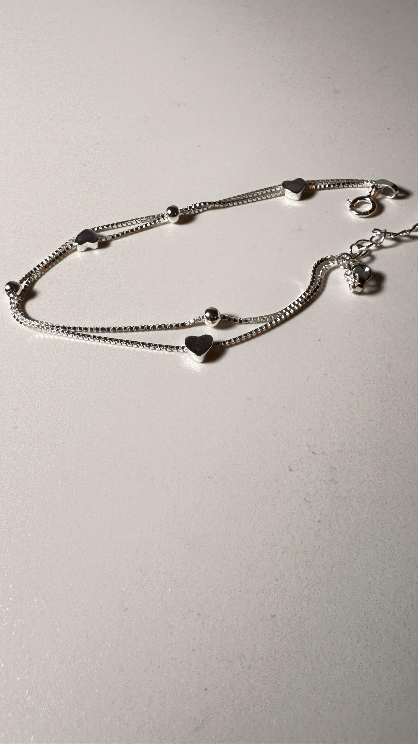 Sterling silver bracelet with heart charms and beads on a light background