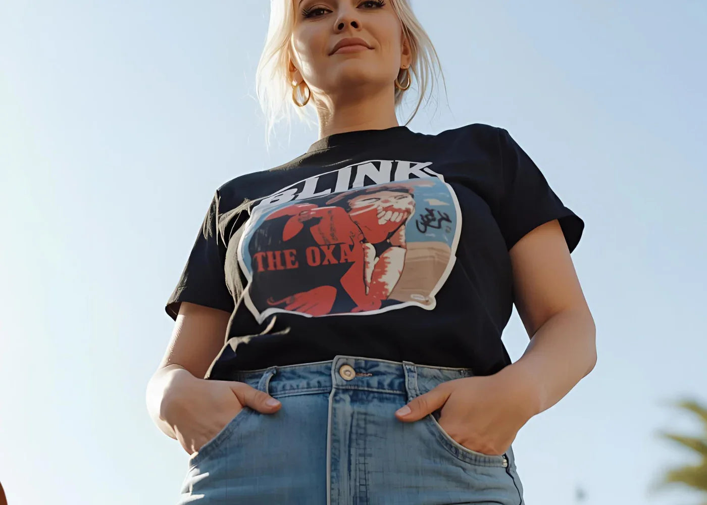 Woman in black Blink graphic t-shirt and light blue jeans posing outdoors under clear sky