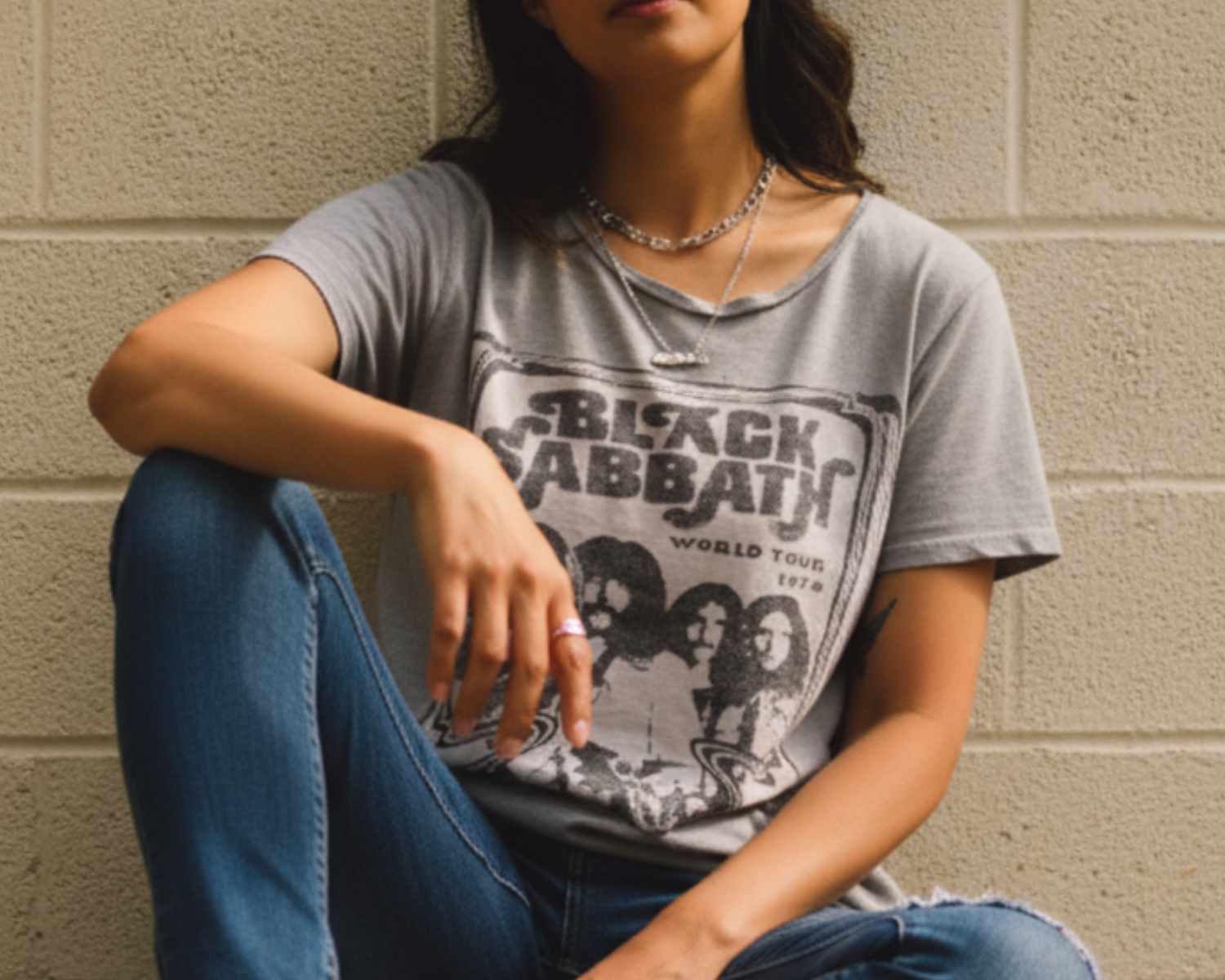 Woman wearing Black Sabbath band t-shirt and ripped jeans sitting by a beige wall
