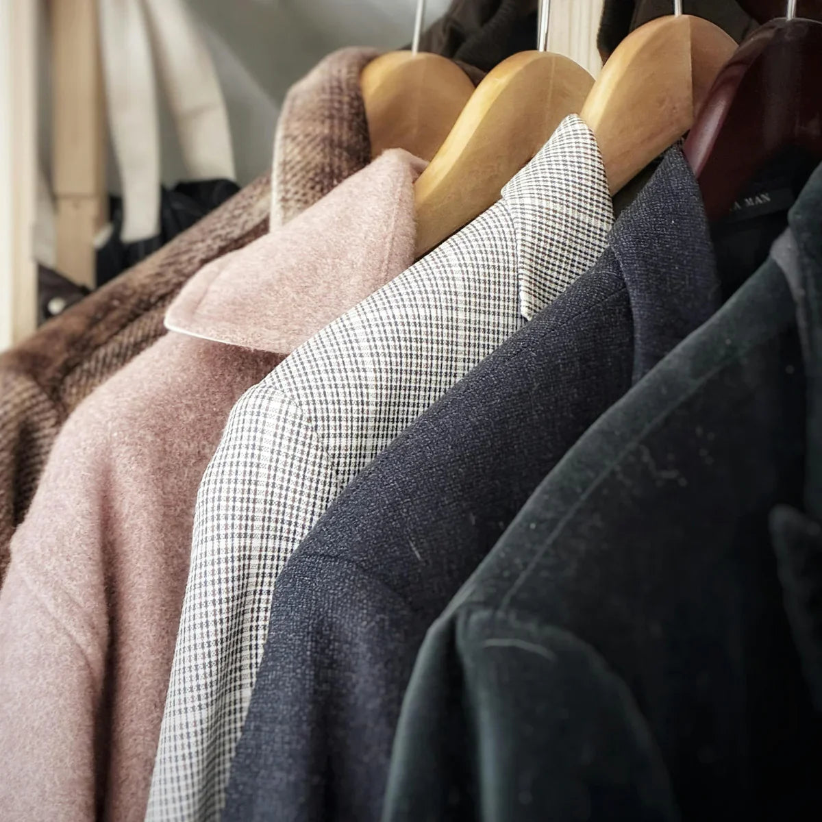 Wool and tweed blazers on wooden hangers in a closet