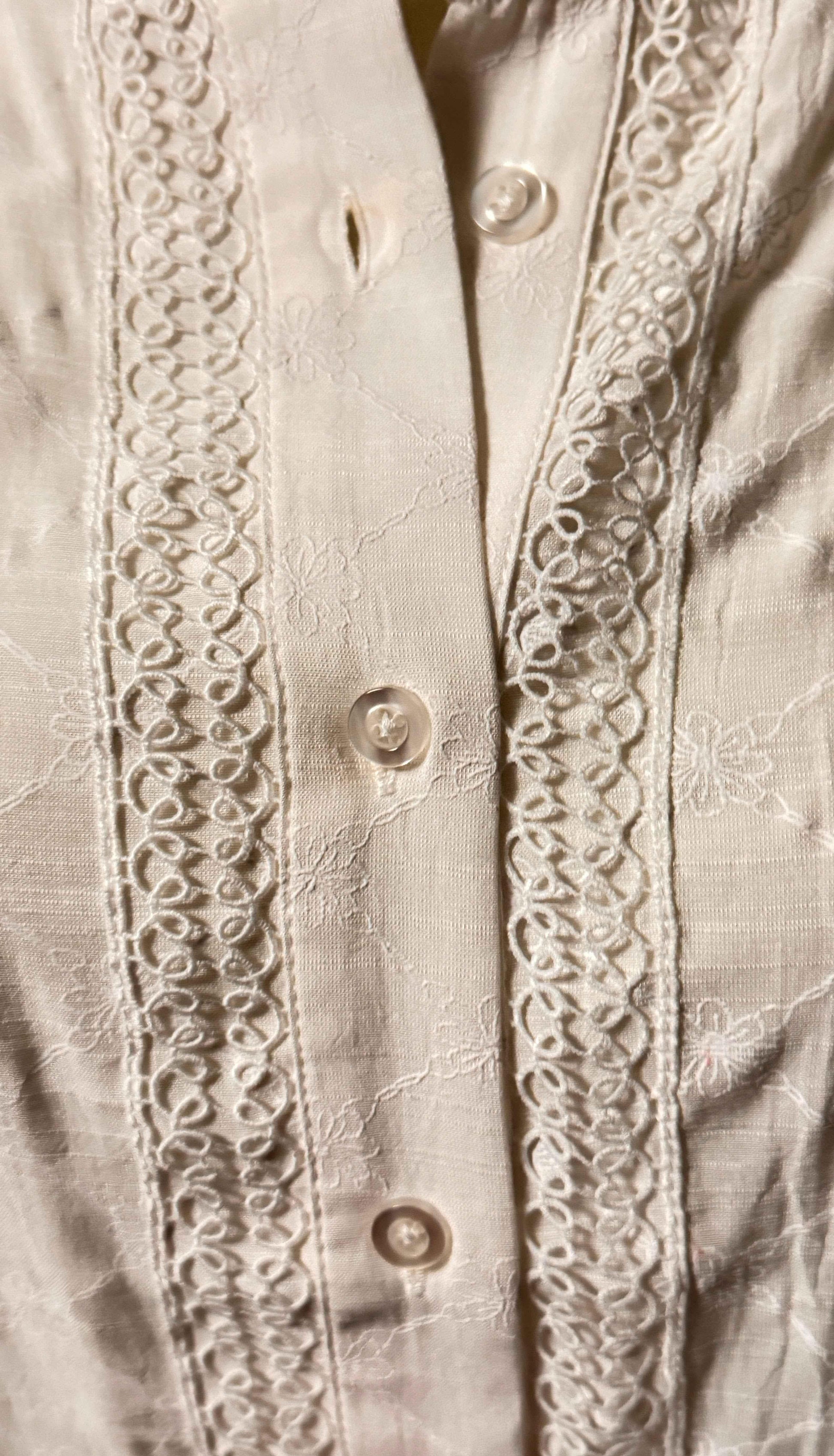 Cream blouse with floral embroidery, lace trim, and pearl buttons, close-up detail