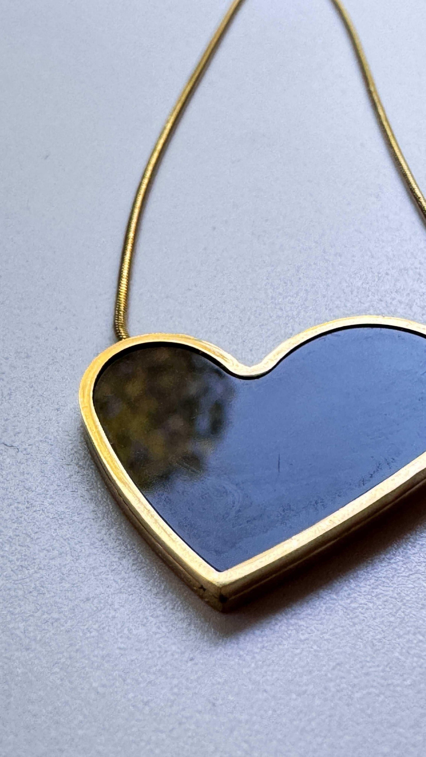Gold heart-shaped pendant necklace with dark center on textured light surface