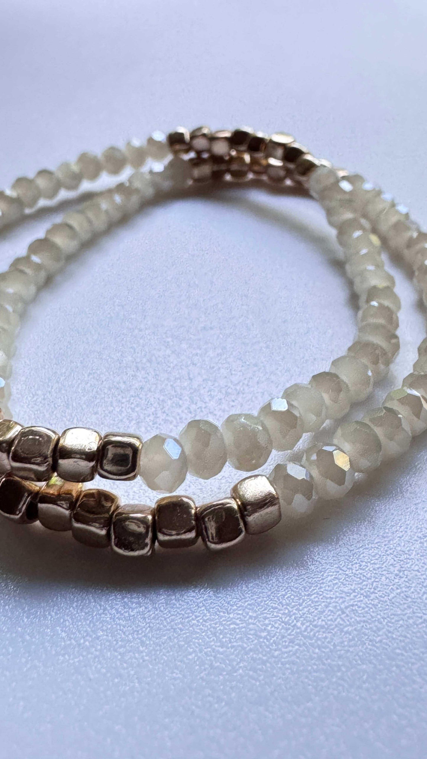 Beige sparkle beaded bracelet with metallic gold beads on a smooth white surface