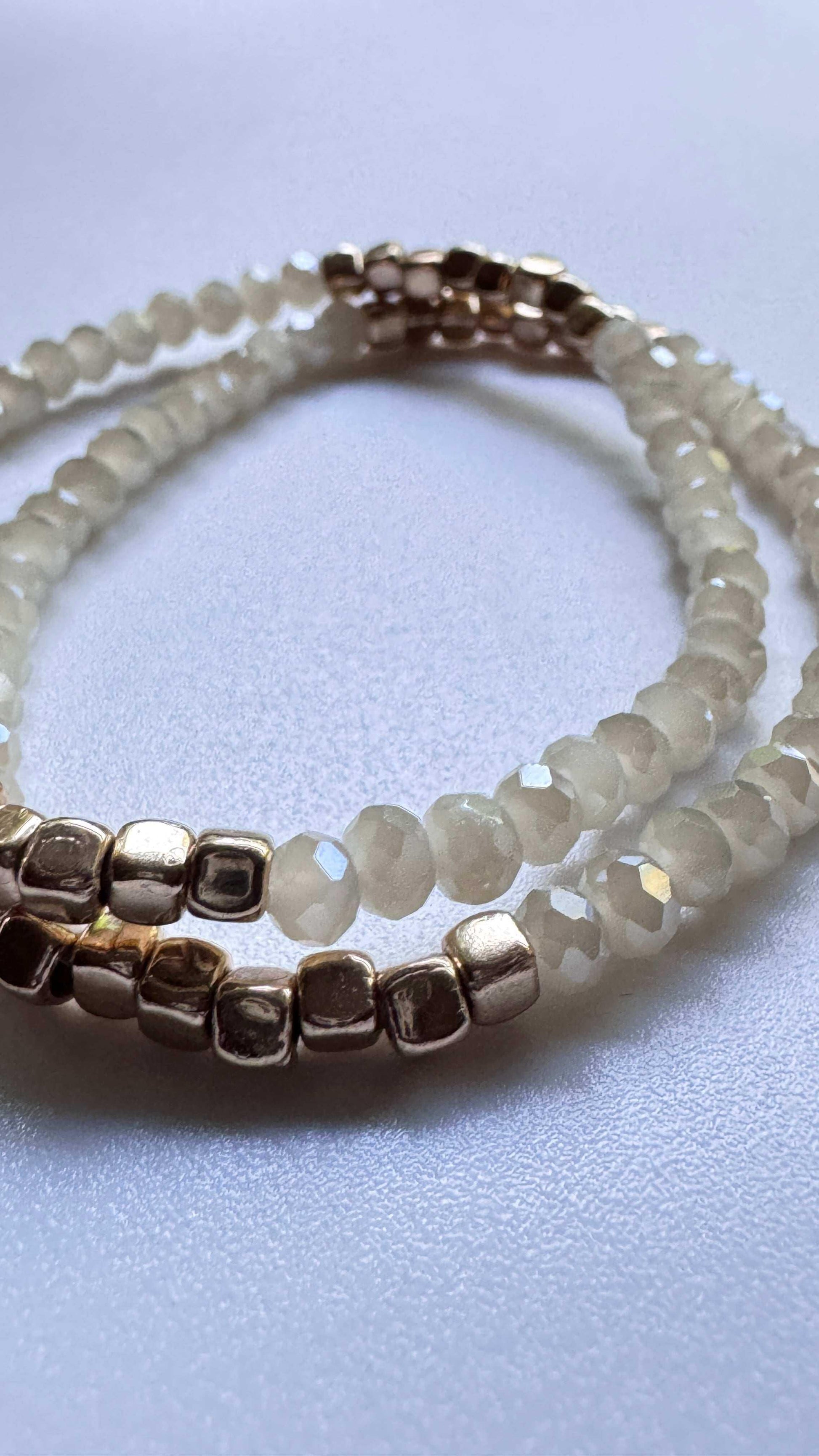 Beige sparkle beaded bracelet with metallic gold beads on a smooth white surface