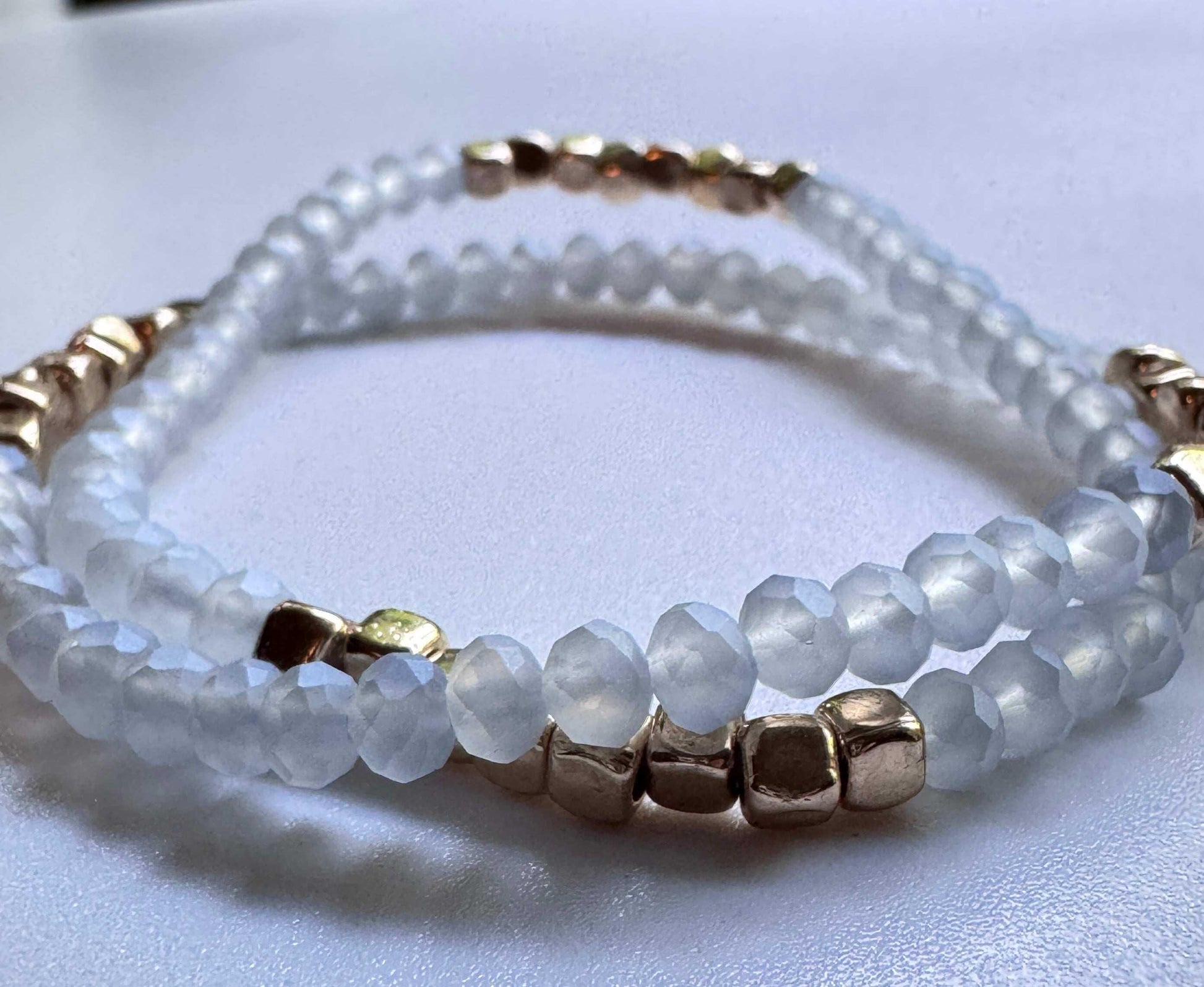 White beaded bracelet with gold square beads on a smooth white surface
