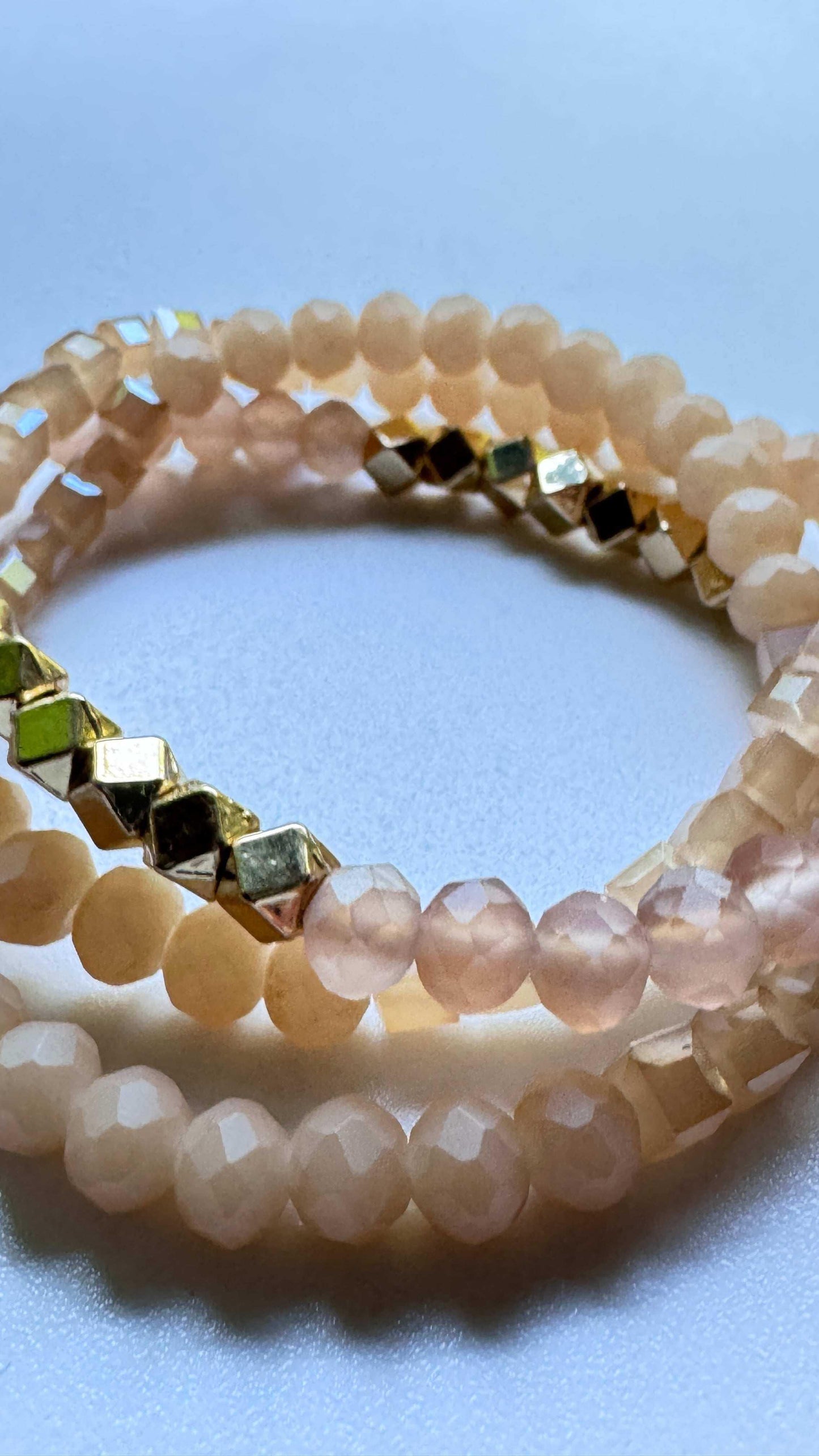 Stack of pastel beaded bracelets with faceted gold and peach beads on white surface