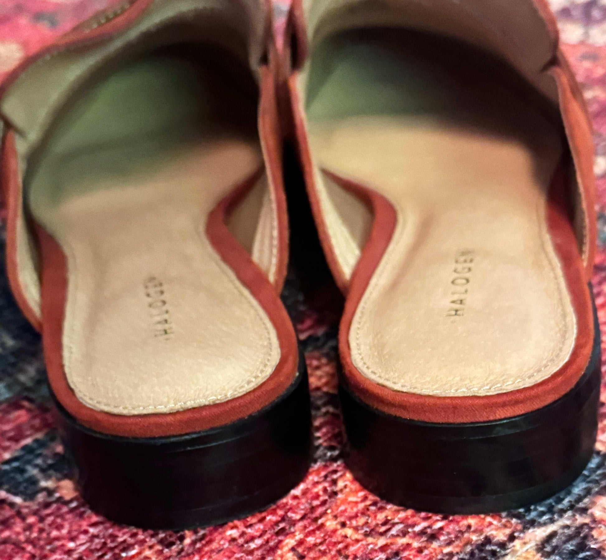 Burnt orange suede mules with cushioned insoles on a multicolored textured rug