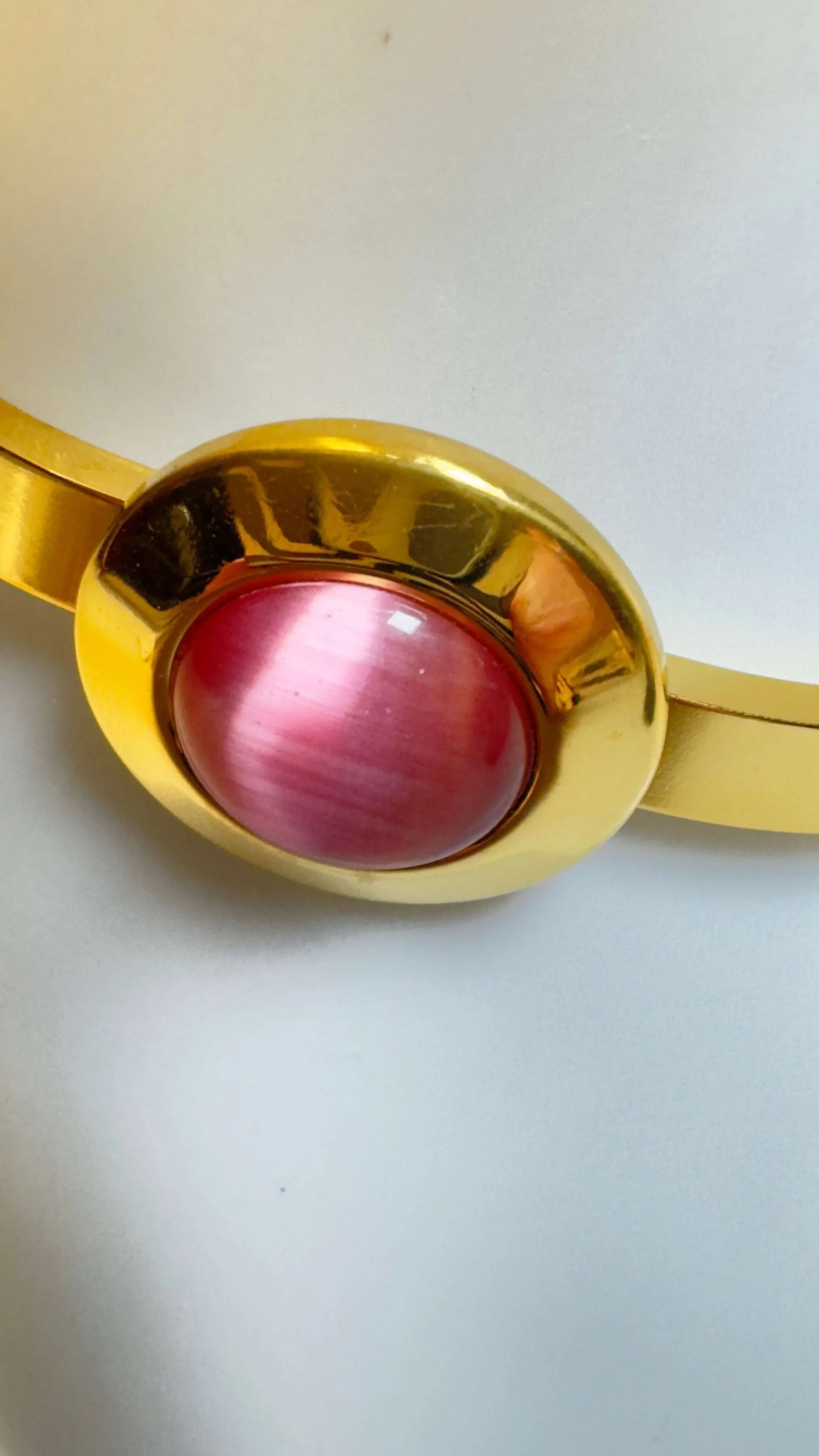 Gold bangle bracelet with oval pink stone on white background