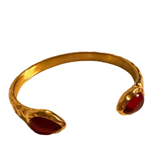 Gold bracelet with textured finish and two red stone accents on white background