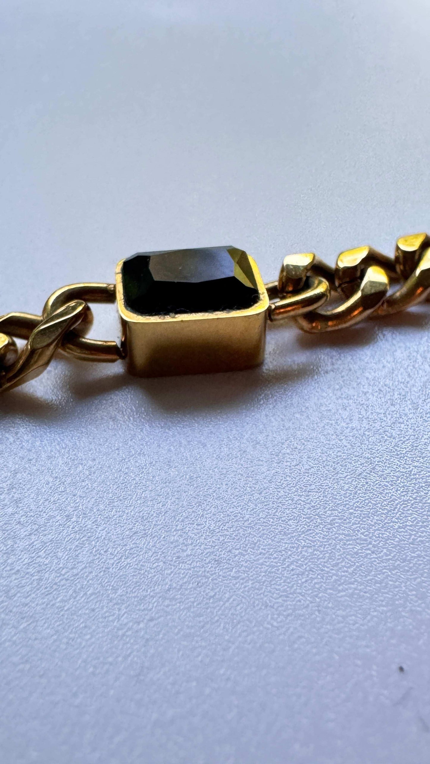 Gold chain bracelet with a rectangular black gemstone on a light background