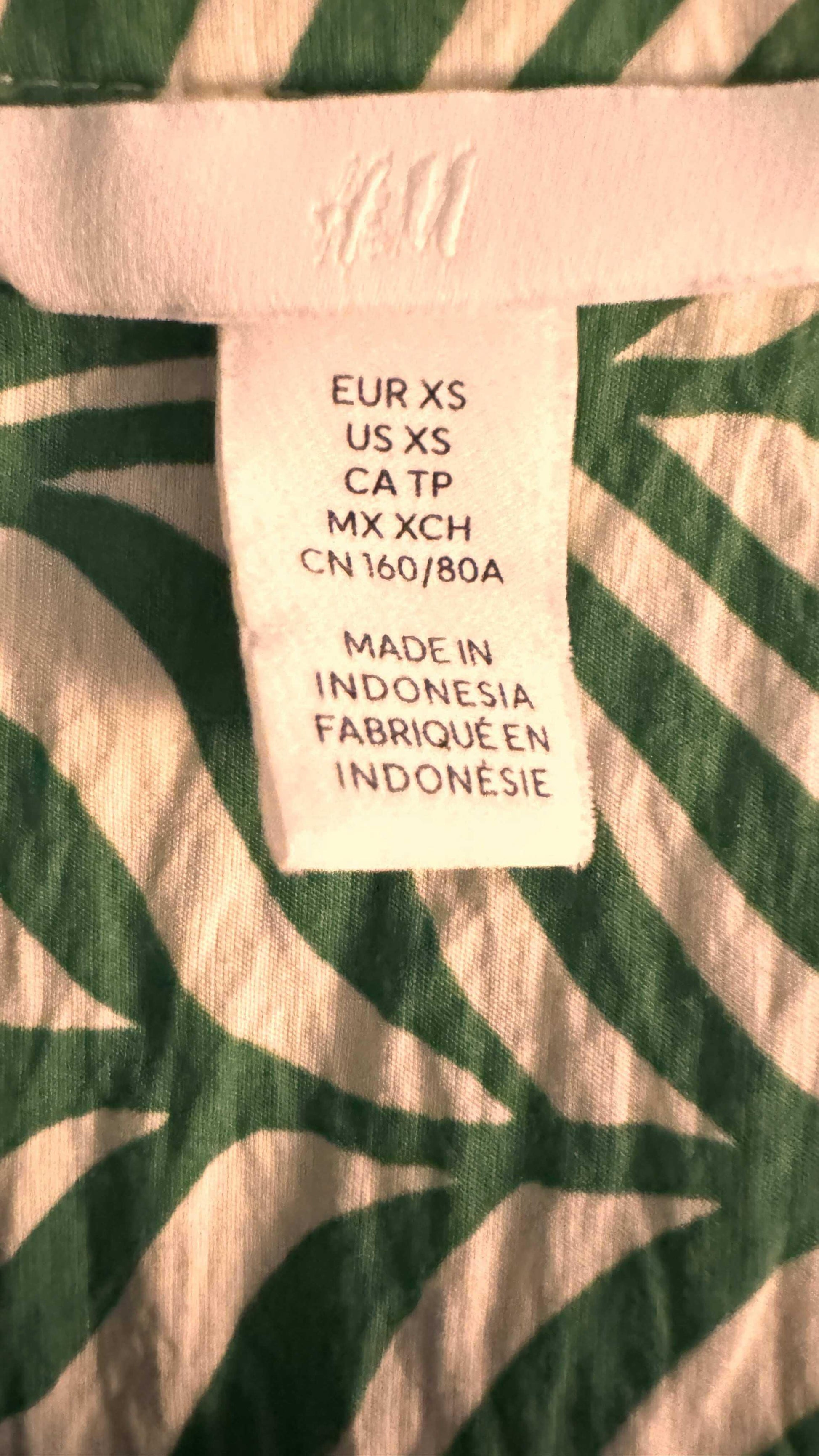 H&M blouse size tag, XS, made in Indonesia, with green and white fabric pattern visible