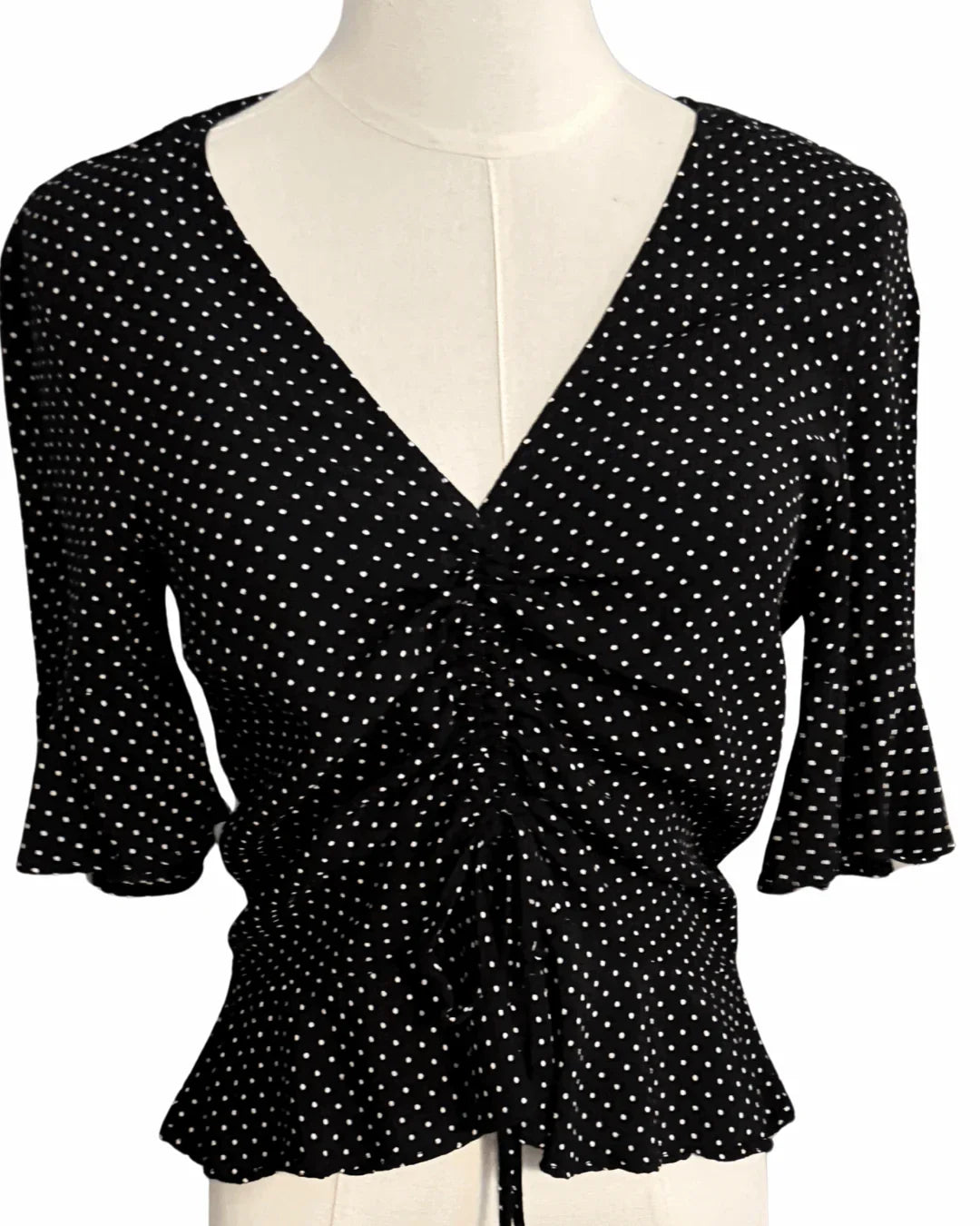 Black polka dot blouse with V-neck and ruched front on mannequin