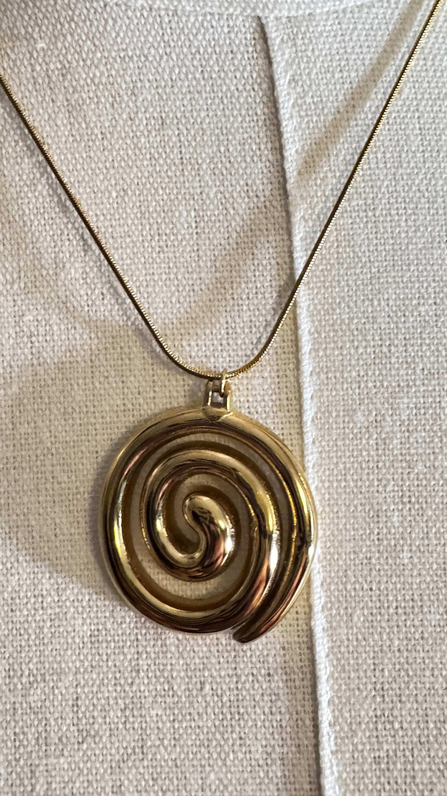 Gold spiral pendant necklace on textured beige fabric background