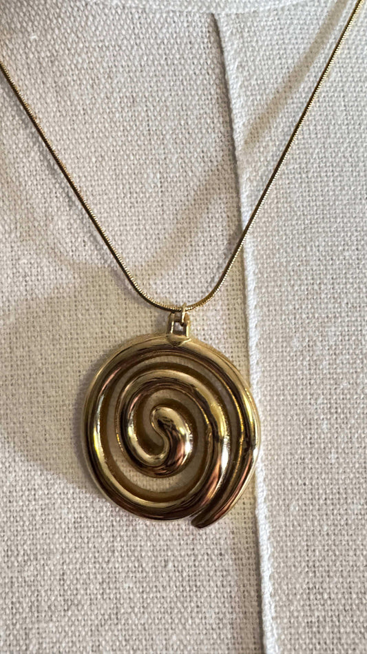 Gold spiral pendant necklace on textured beige fabric background