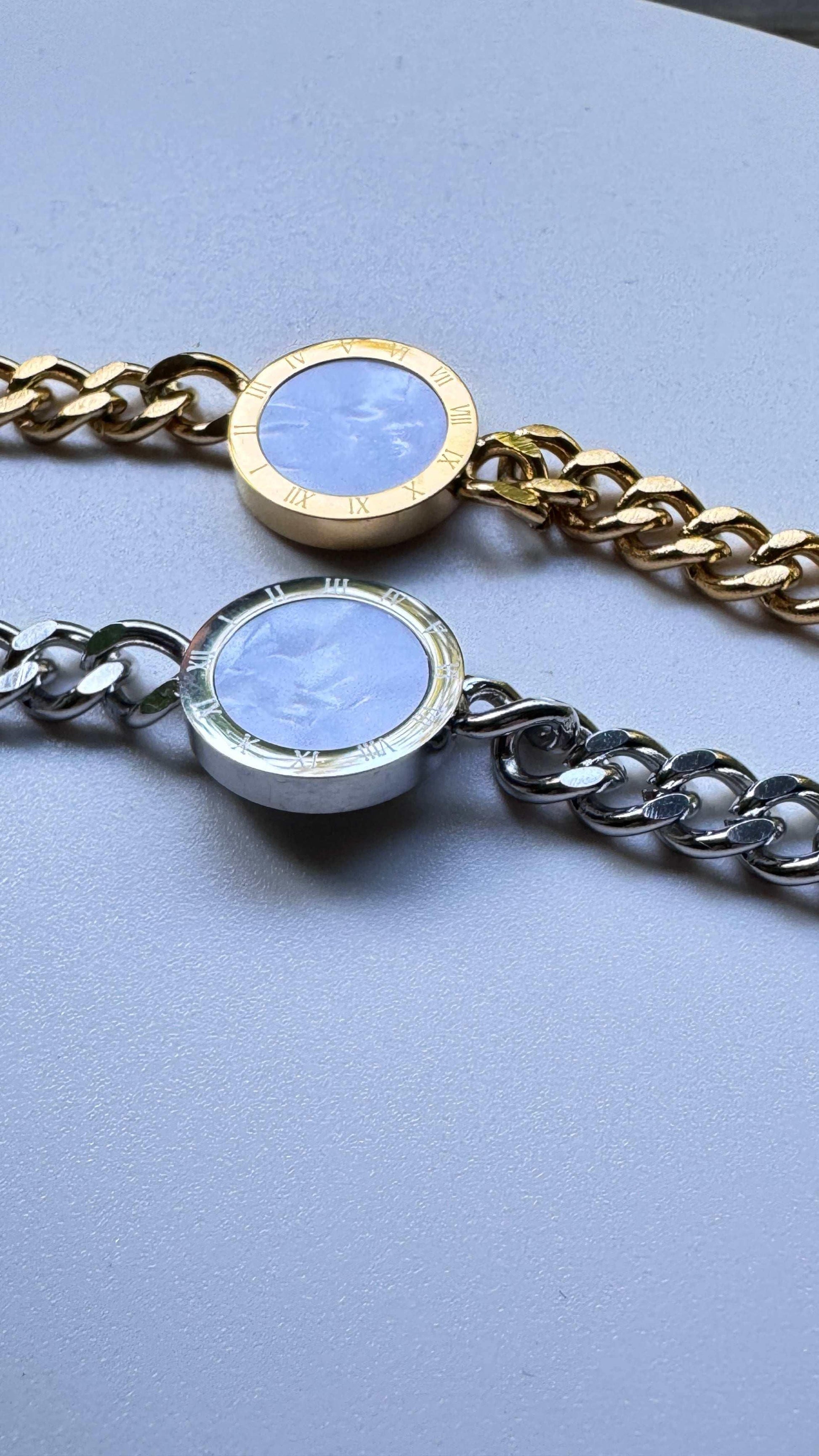 Gold and silver chain bracelets with round roman numeral stone charms on a light surface