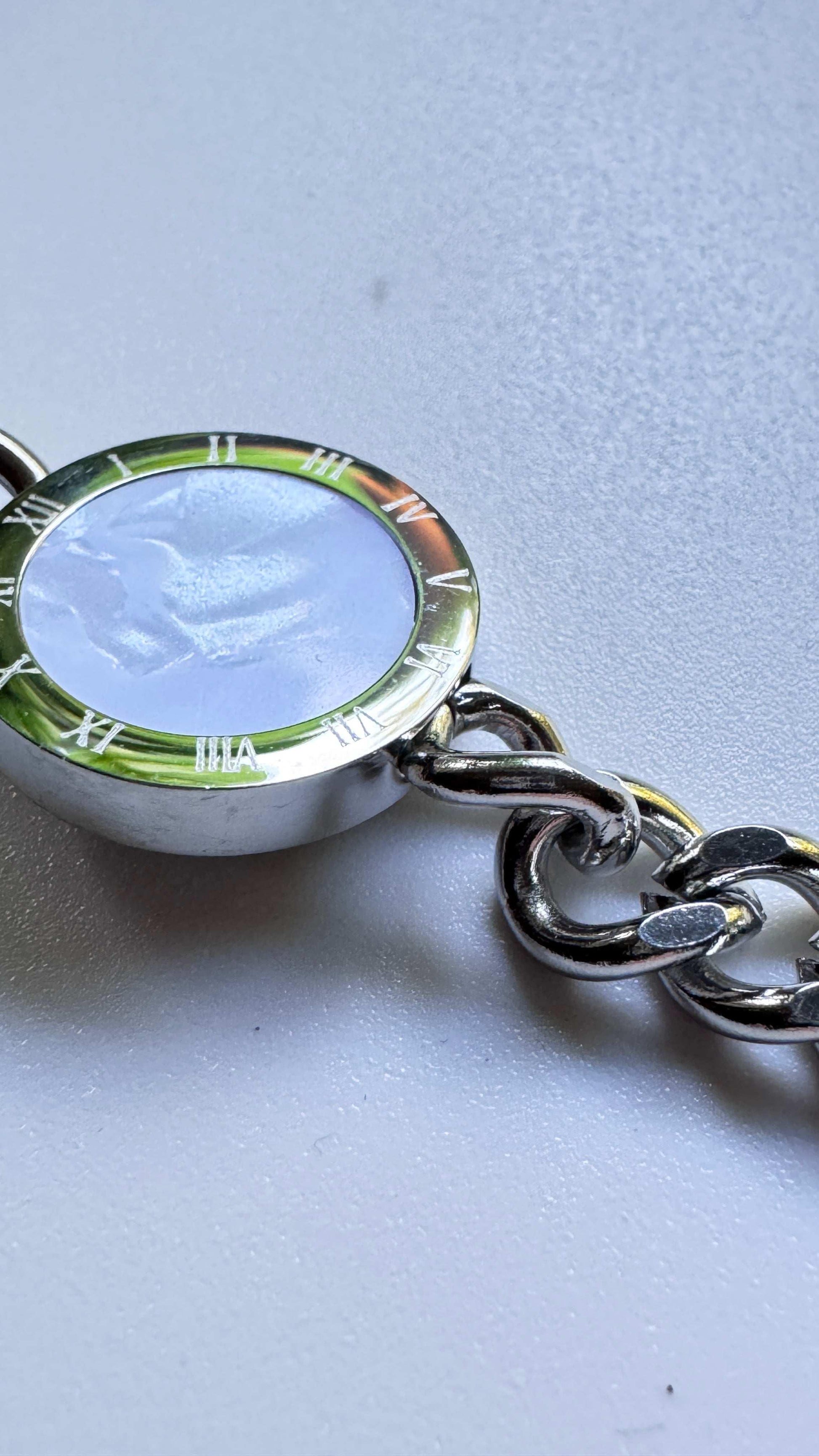 Close-up of a silver round reflective bracelet with Roman numerals on a white surface
