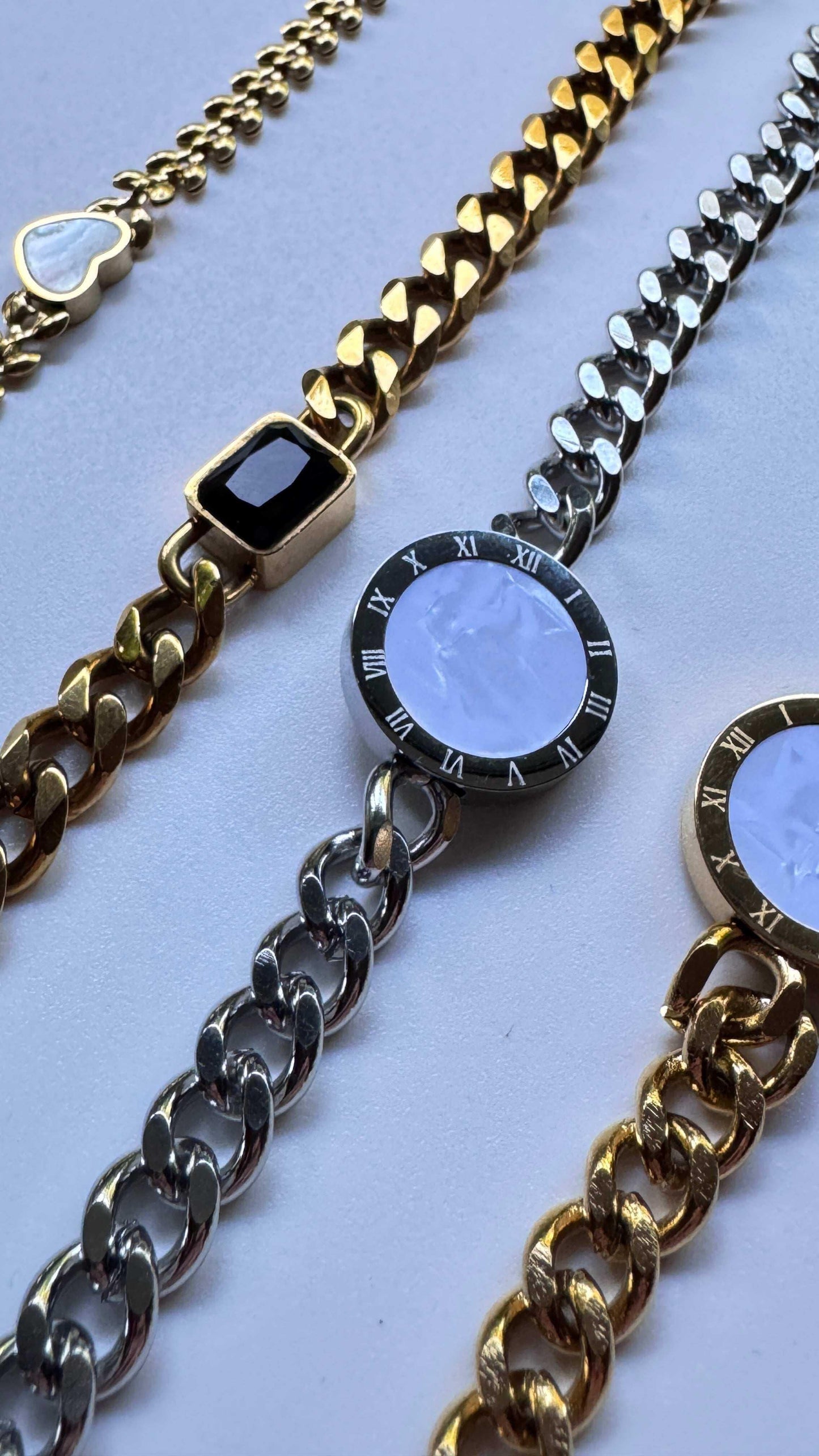 Elegant gold and silver stone bracelets with heart and round Roman numeral charms on white surface