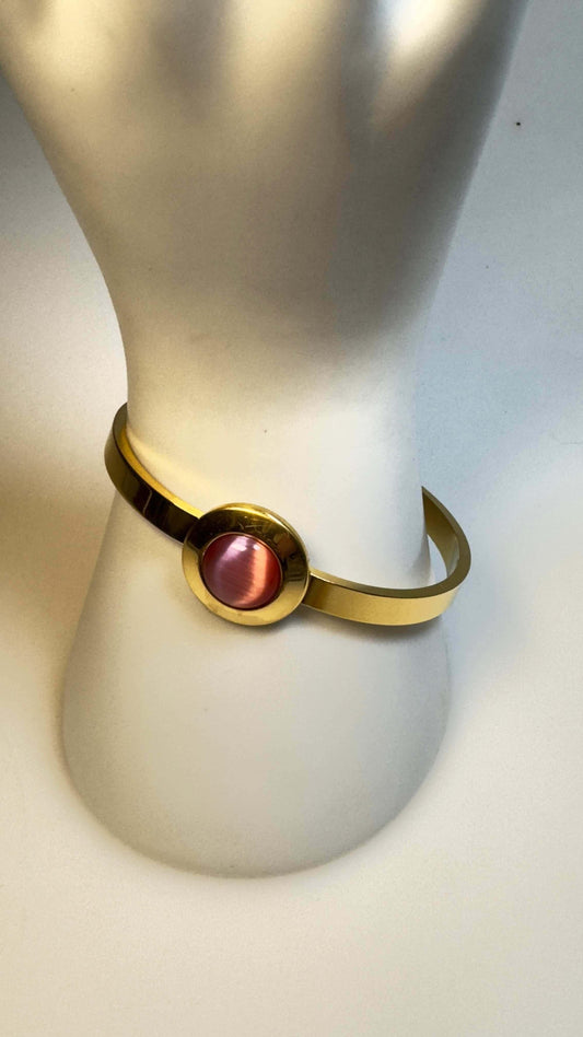 Gold bracelet with pink stone centerpiece on a white display stand
