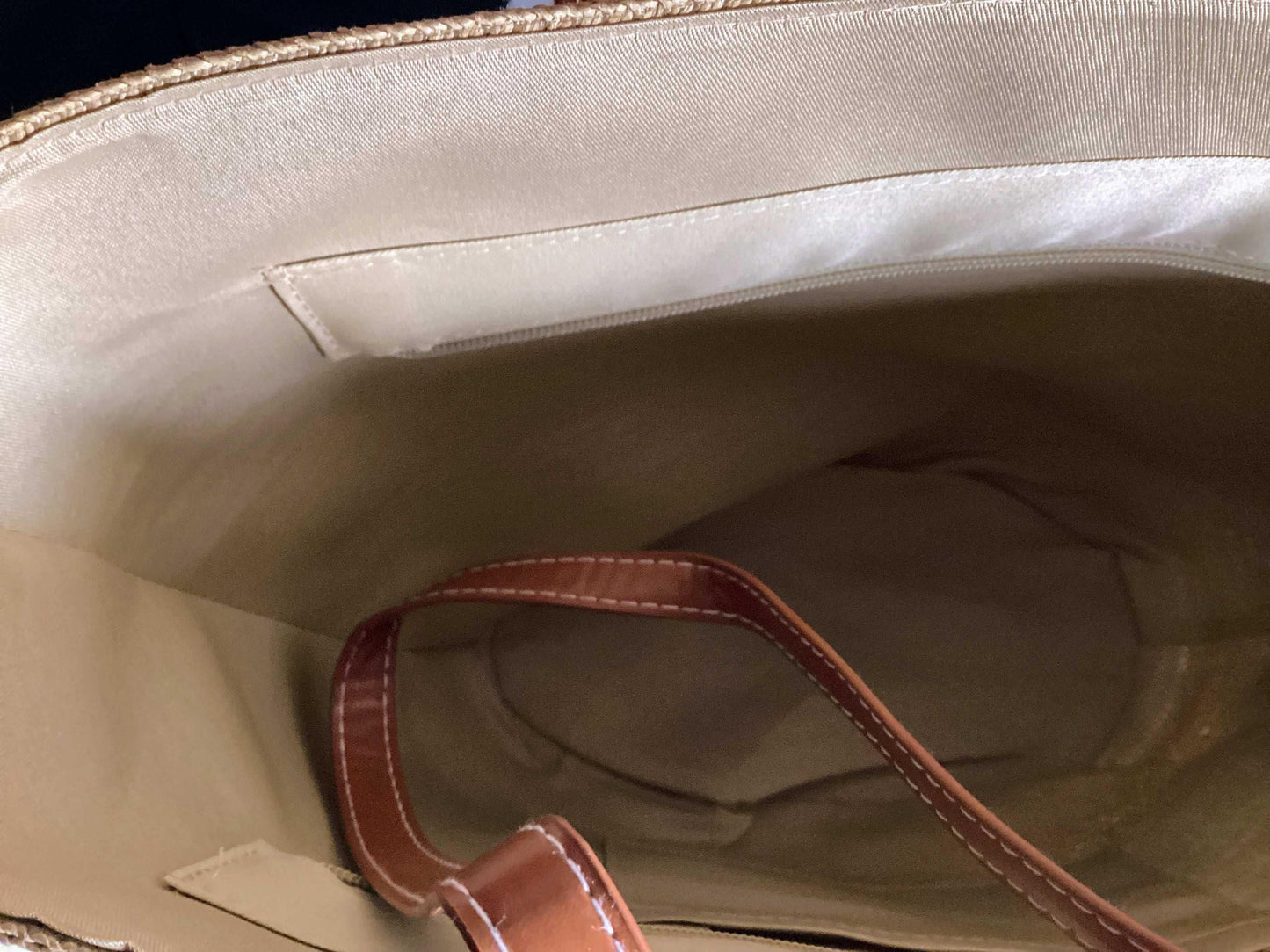 Interior of straw beach bag with tan lining and brown leather strap, summer accessory