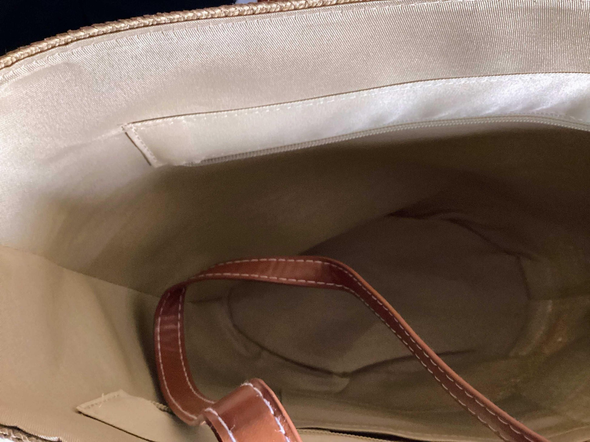Interior of straw beach bag with tan lining and brown leather strap, summer accessory
