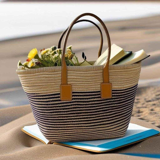 Striped straw beach bag with leather handles, flowers, and books on sand at seaside.