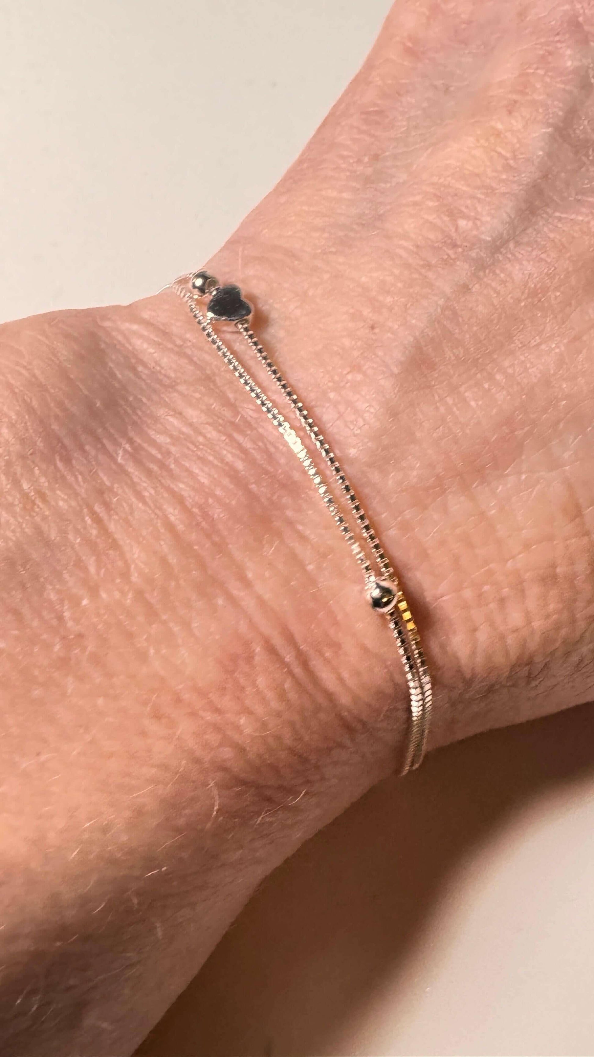 Delicate silver heart bracelet with double chain detail on a wrist