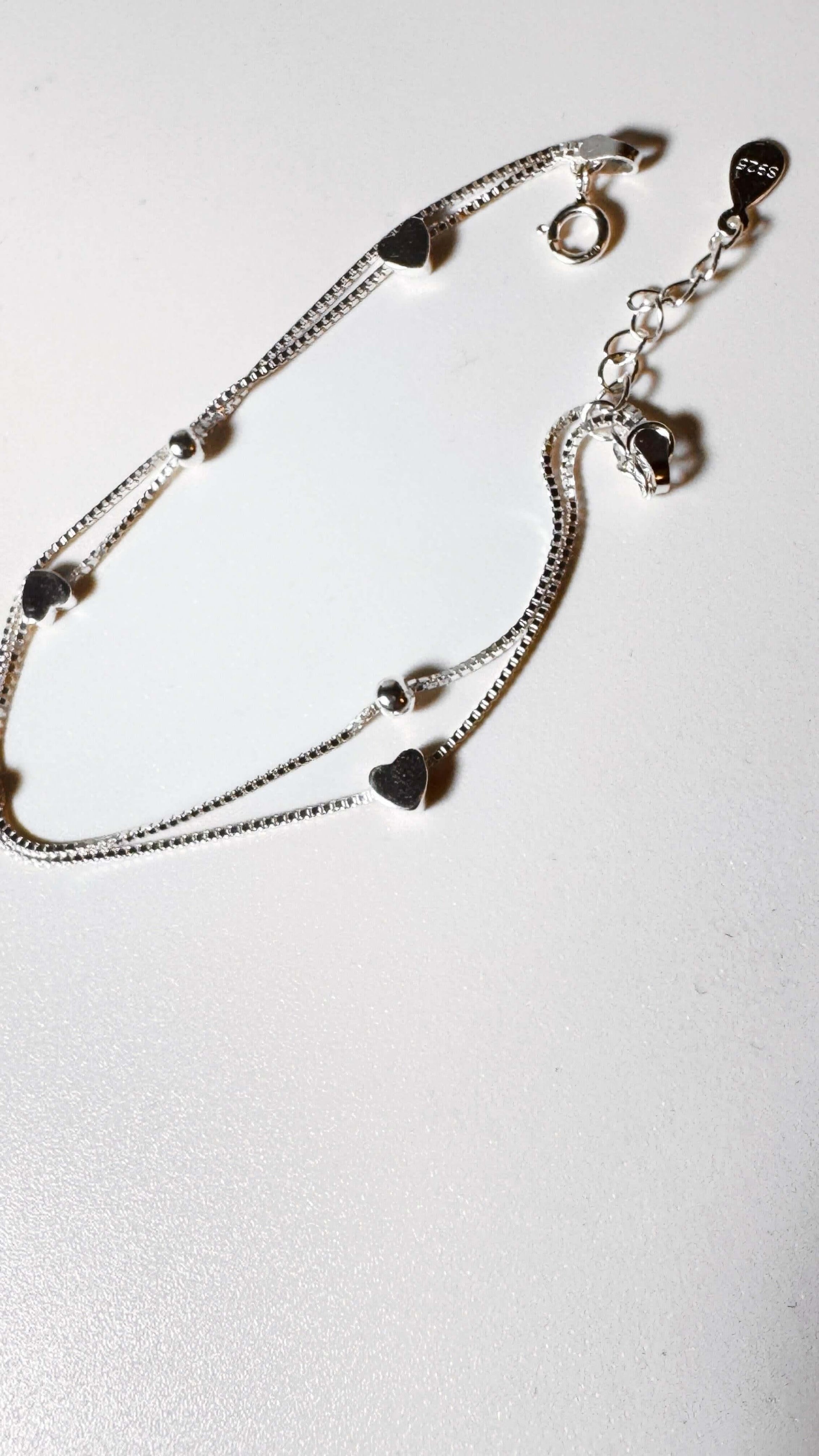 Sterling silver double chain bracelet with heart charms on white background