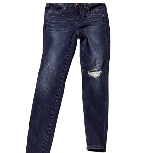 Dark wash distressed skinny jeans with ripped knee and faded details on white background