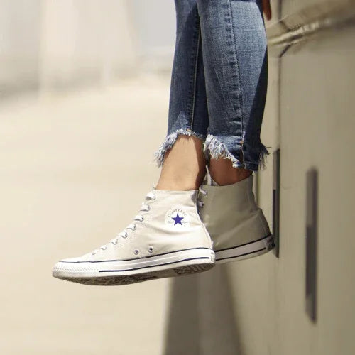 Person wearing beige Converse sneakers and frayed jeans sitting on an outdoor ledge