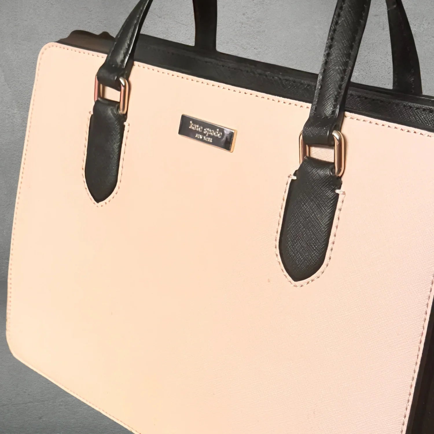 Beige handbag with black handles and gold hardware against gray background