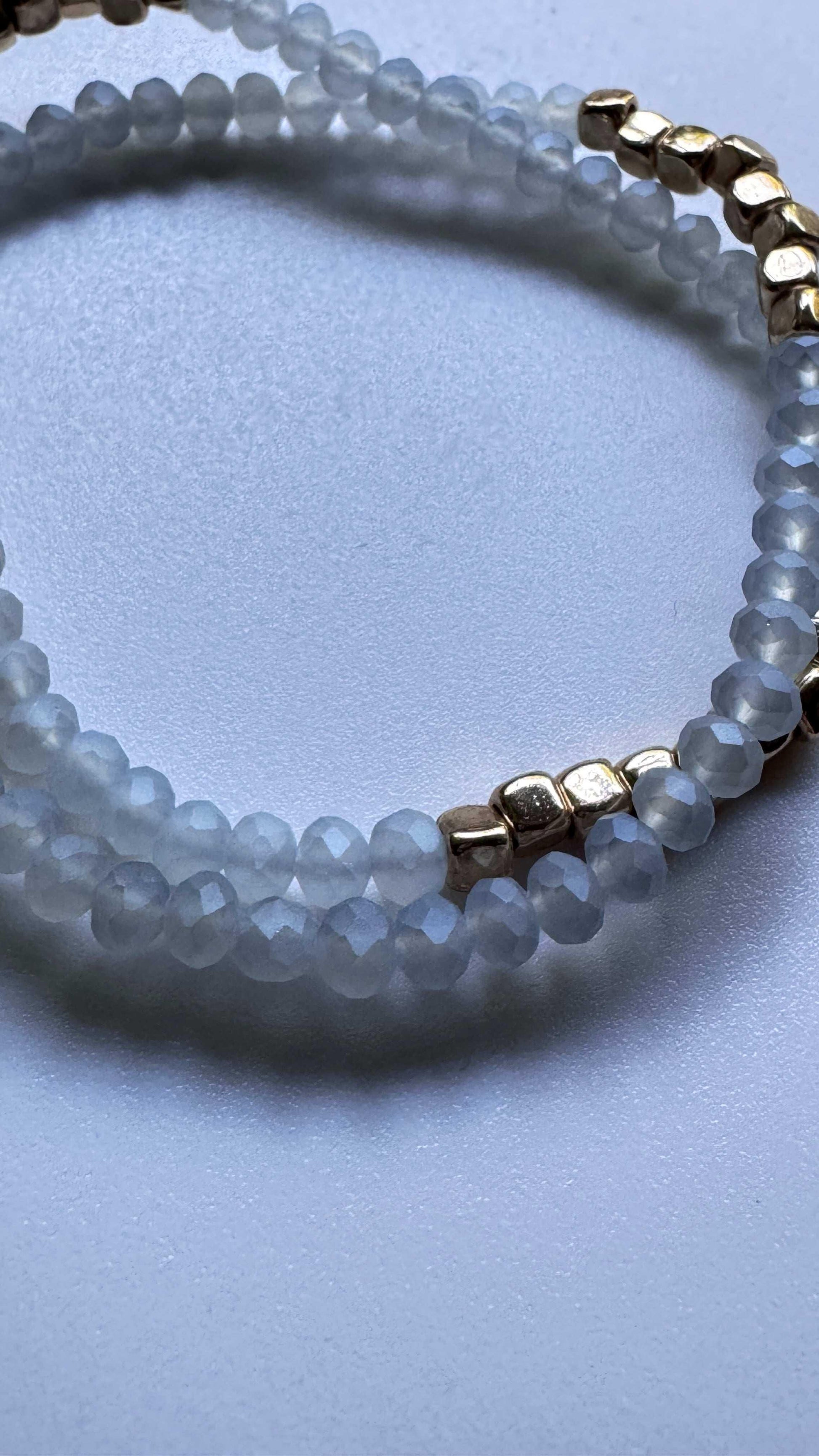 White beaded bracelet with faceted beads and gold accents on a light surface