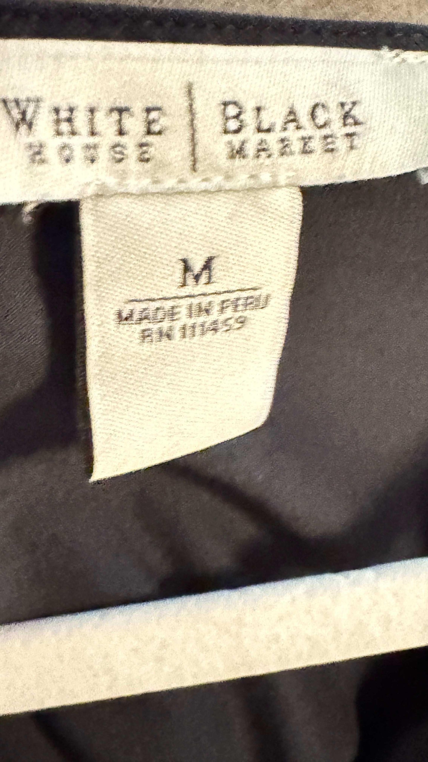White House Black Market blouse clothing tag, size M, made in Peru, on dark fabric