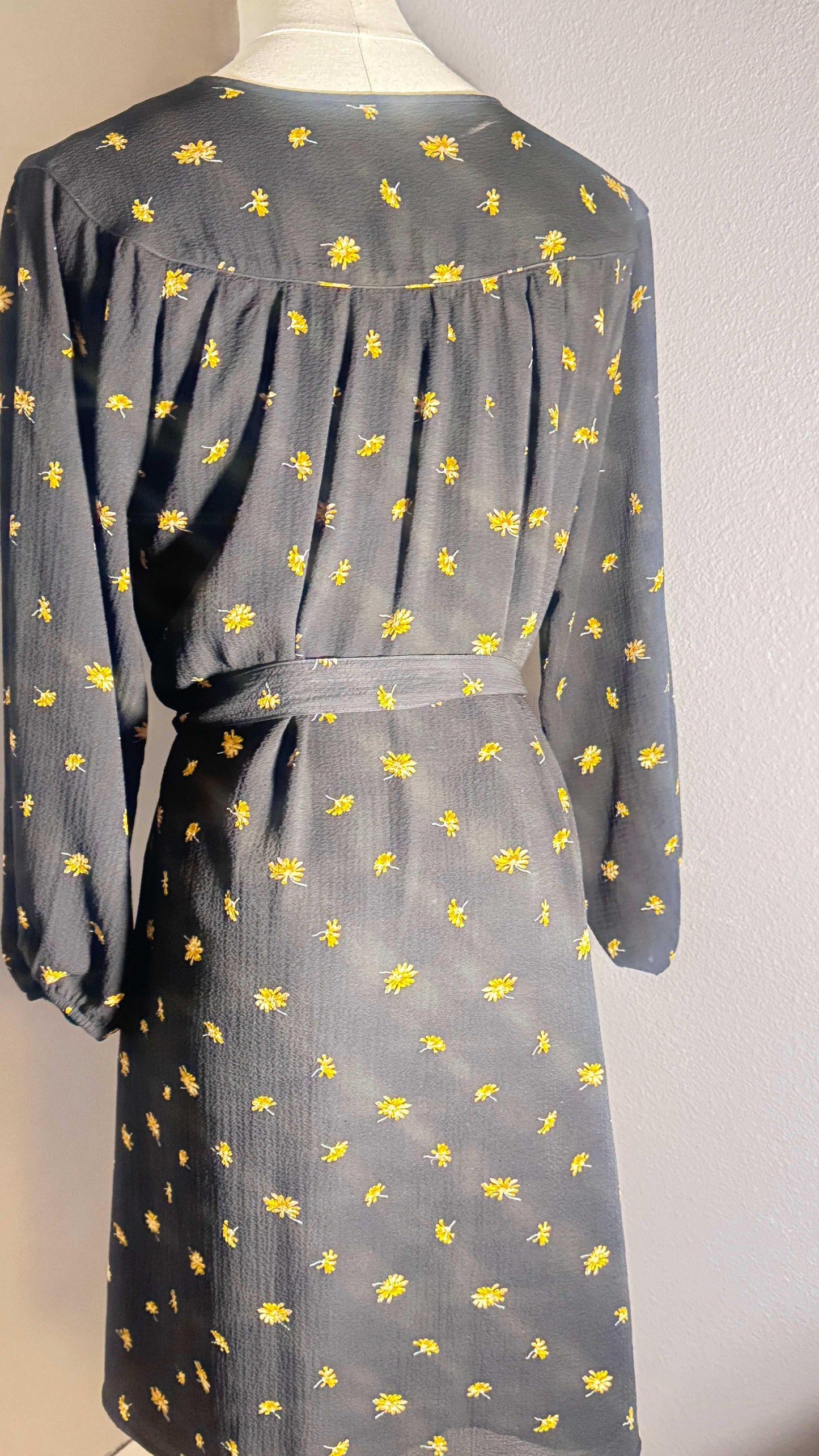 Back view of black floral dress with yellow daisy print and long sleeves on mannequin