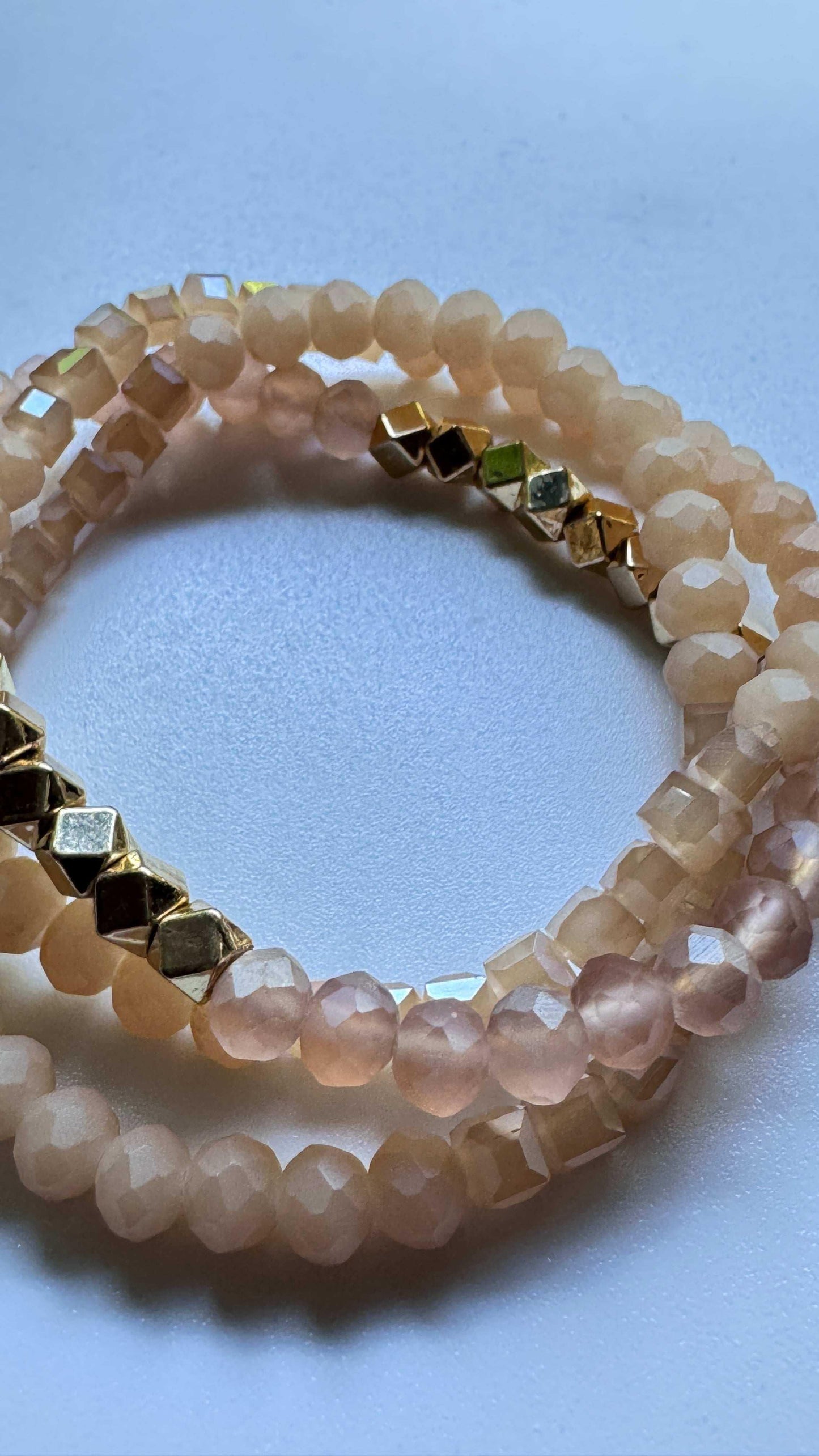 Faceted blush pink beaded bracelet with gold cube accents on white background