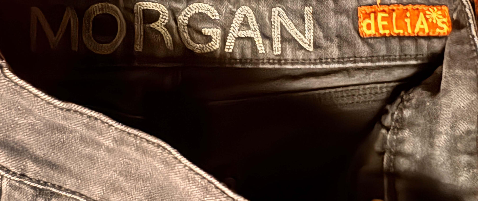Close-up of black denim jeans inner waistband with 'MORGAN' and orange 'dELiA*s' tag