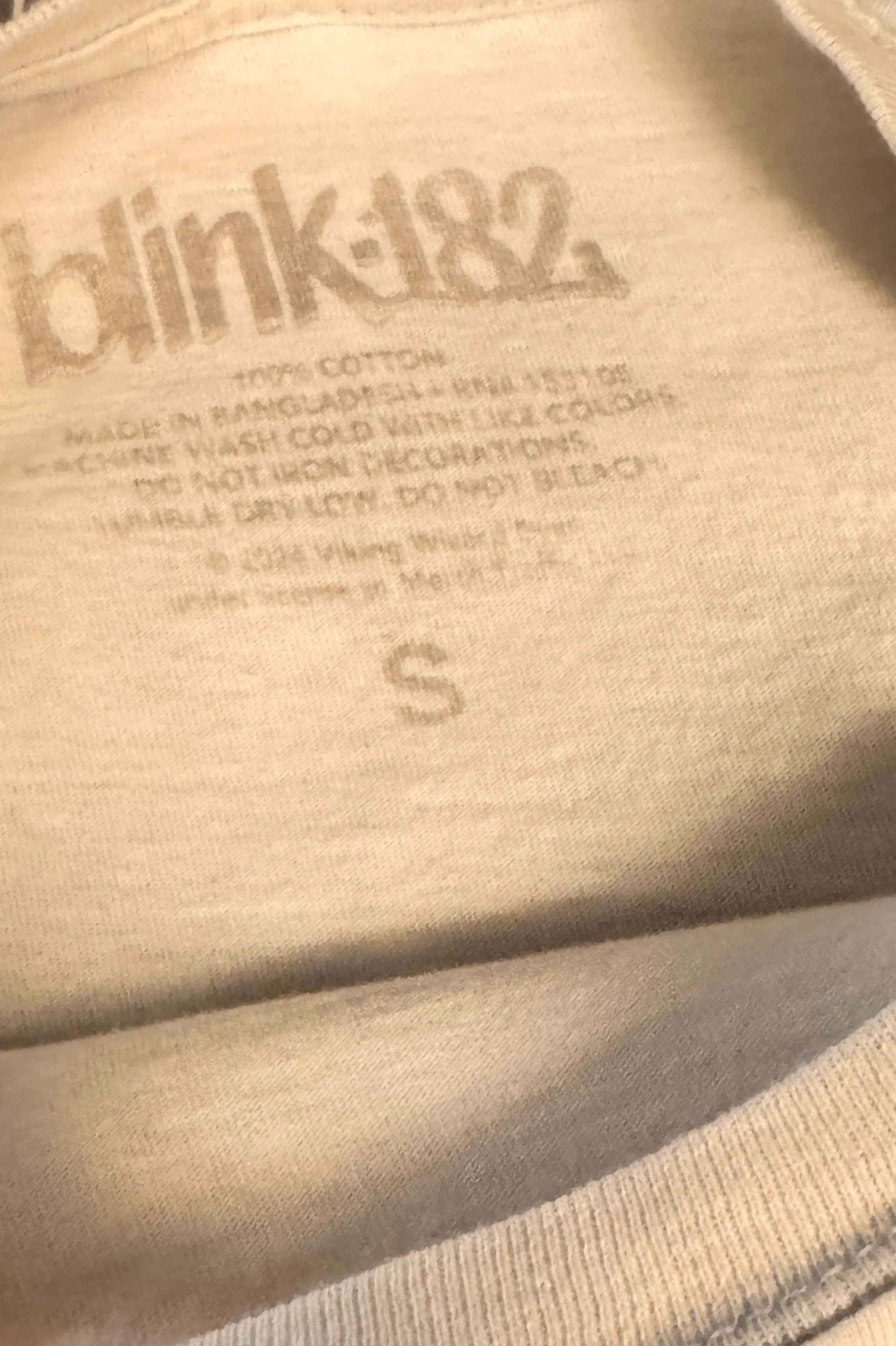 blink-182 vintage band shirt label with printed logo and size S on beige fabric