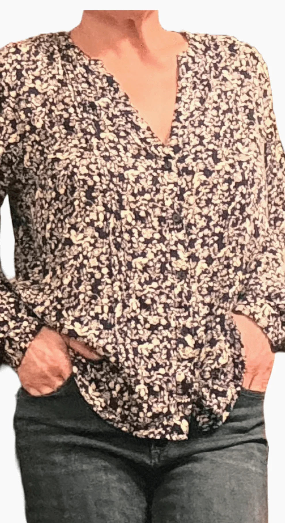 Woman wearing a navy floral blouse and dark jeans with hands in pockets