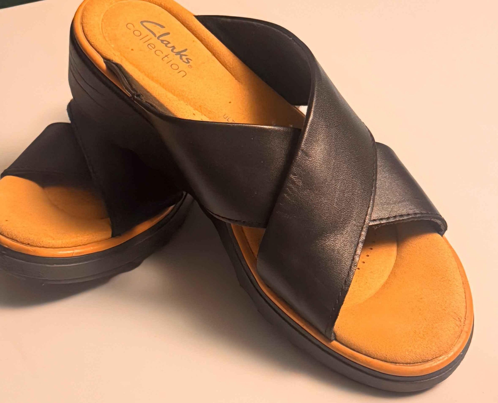 Clarks black leather slide sandals with tan footbed on white background
