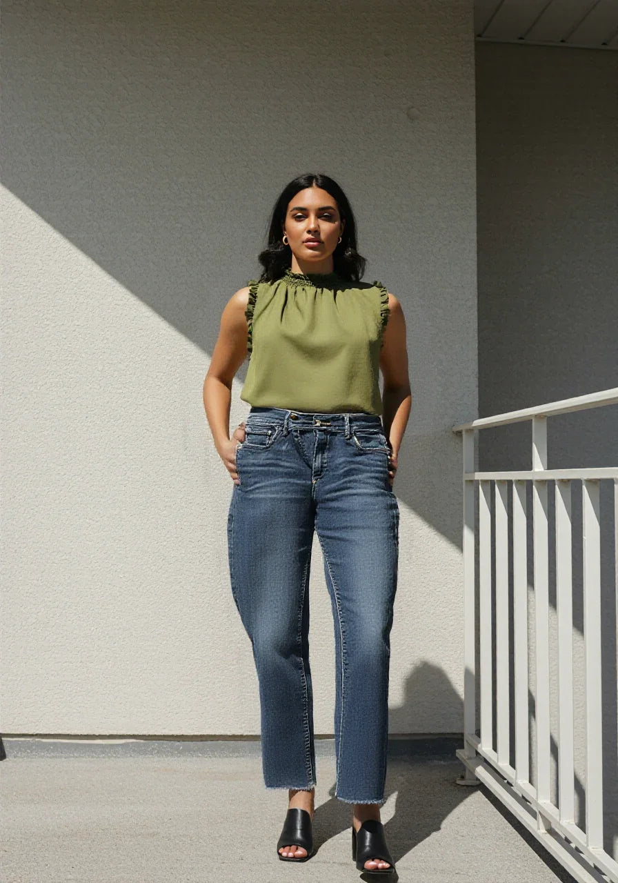 Woman wearing green sleeveless blouse and blue jeans standing on outdoor balcony