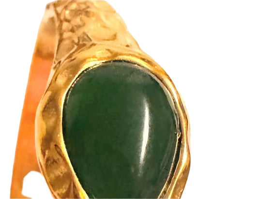 Close-up of a gold bracelet with a polished green stone centerpiece on white background