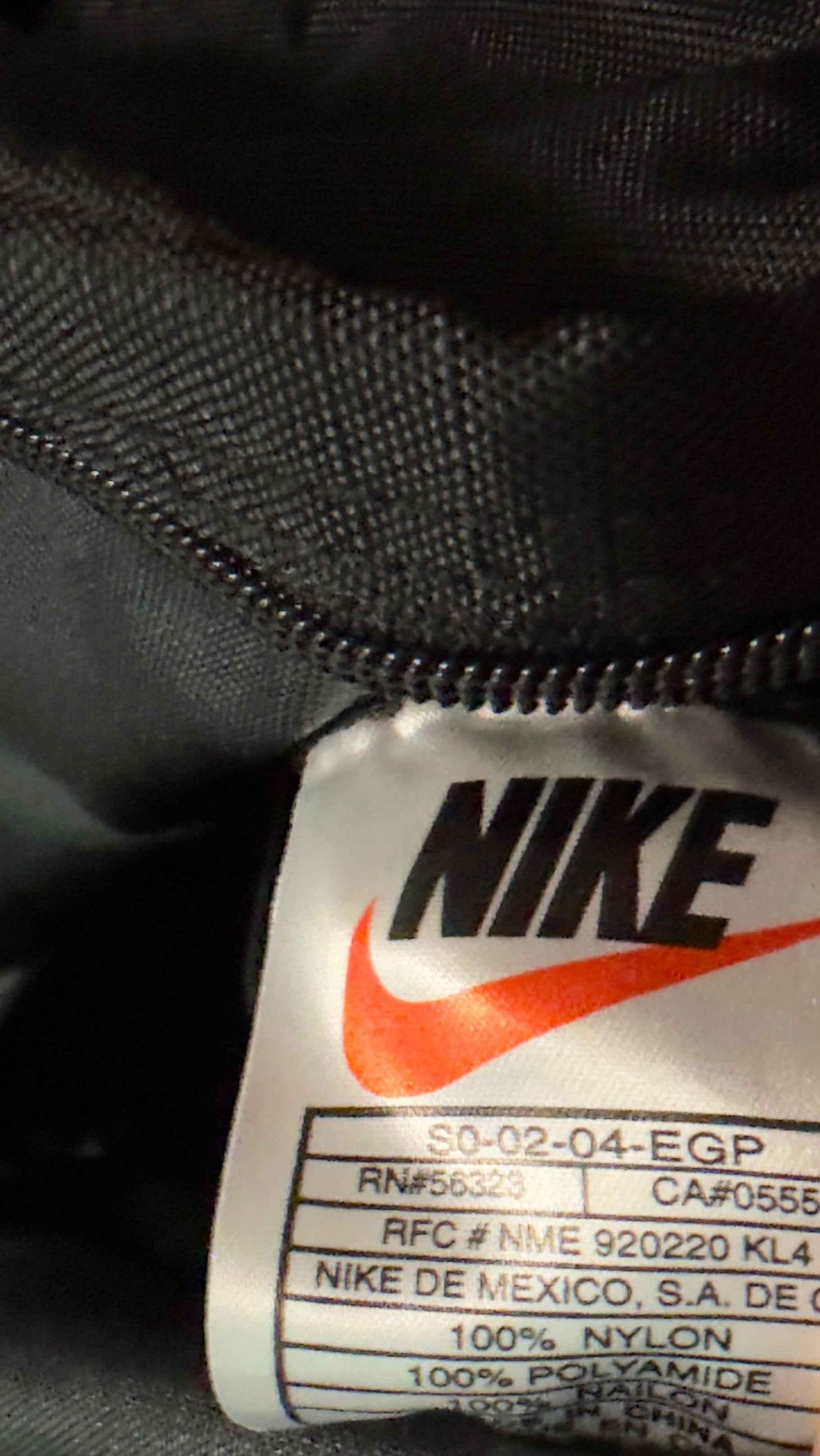 Close-up of black Nike garment tag with red swoosh logo and product details.