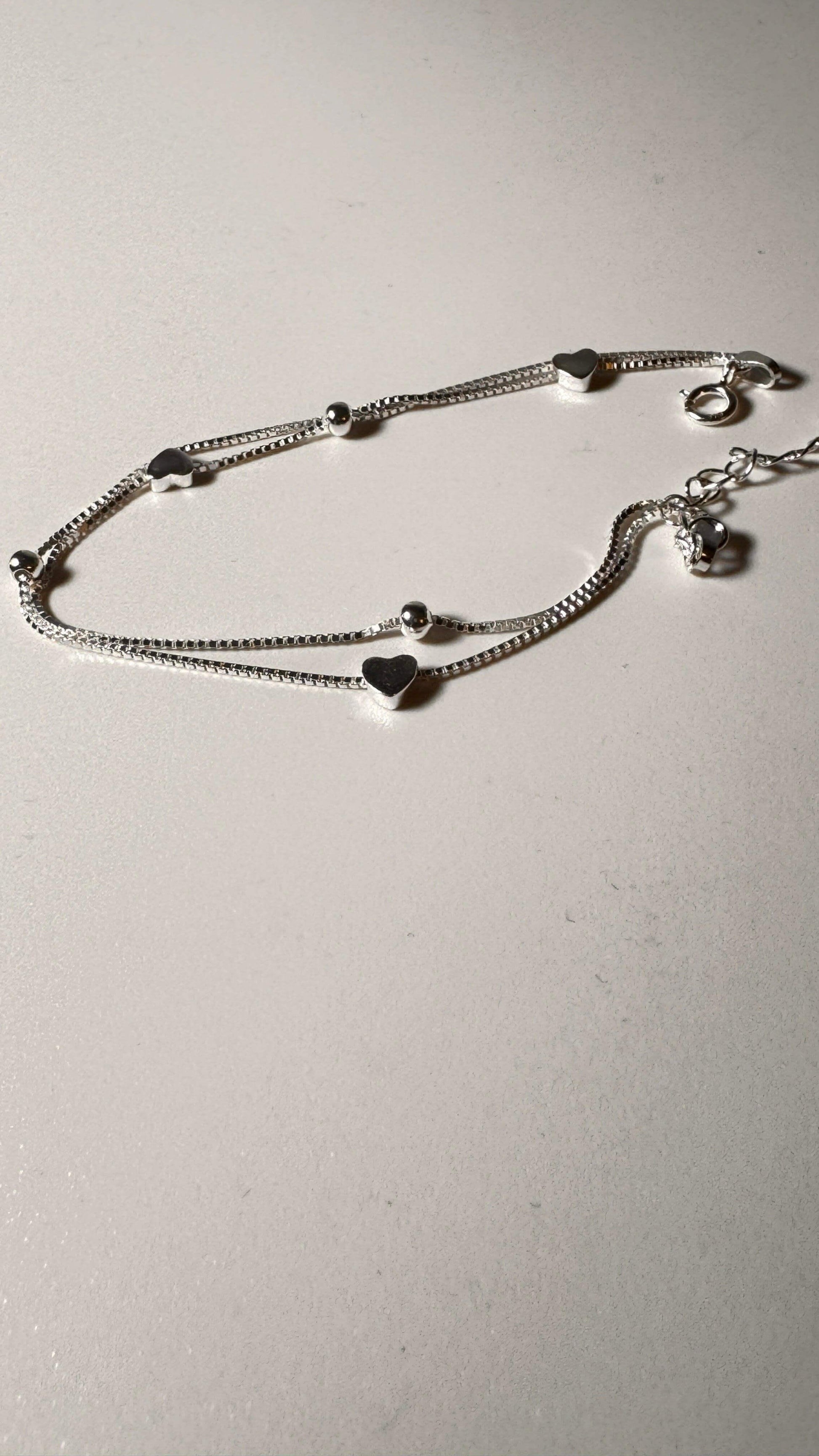 Sterling silver bracelet with heart charms and beads on a light background
