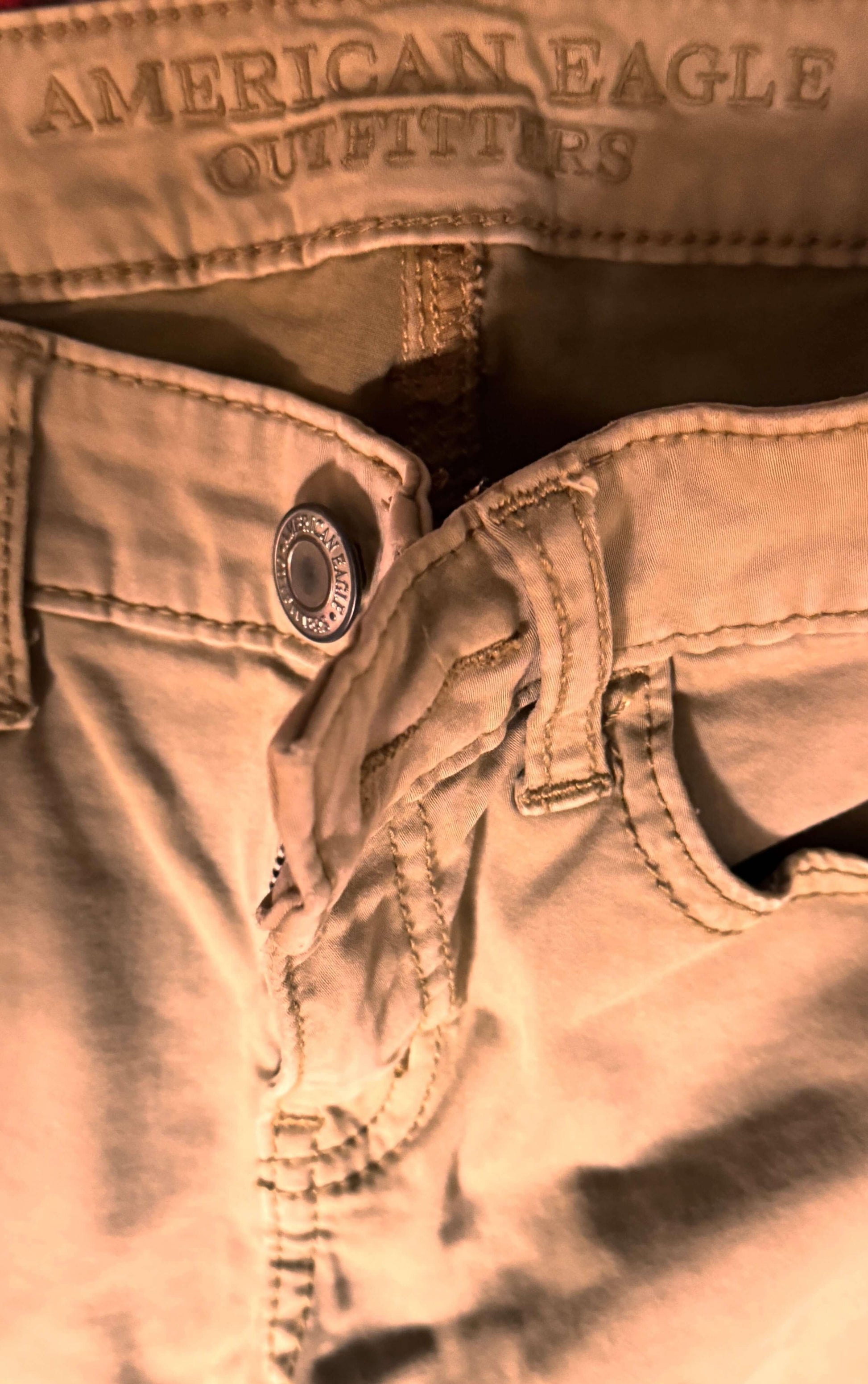 Close-up of tan American Eagle petite denim pants with button and stitched details